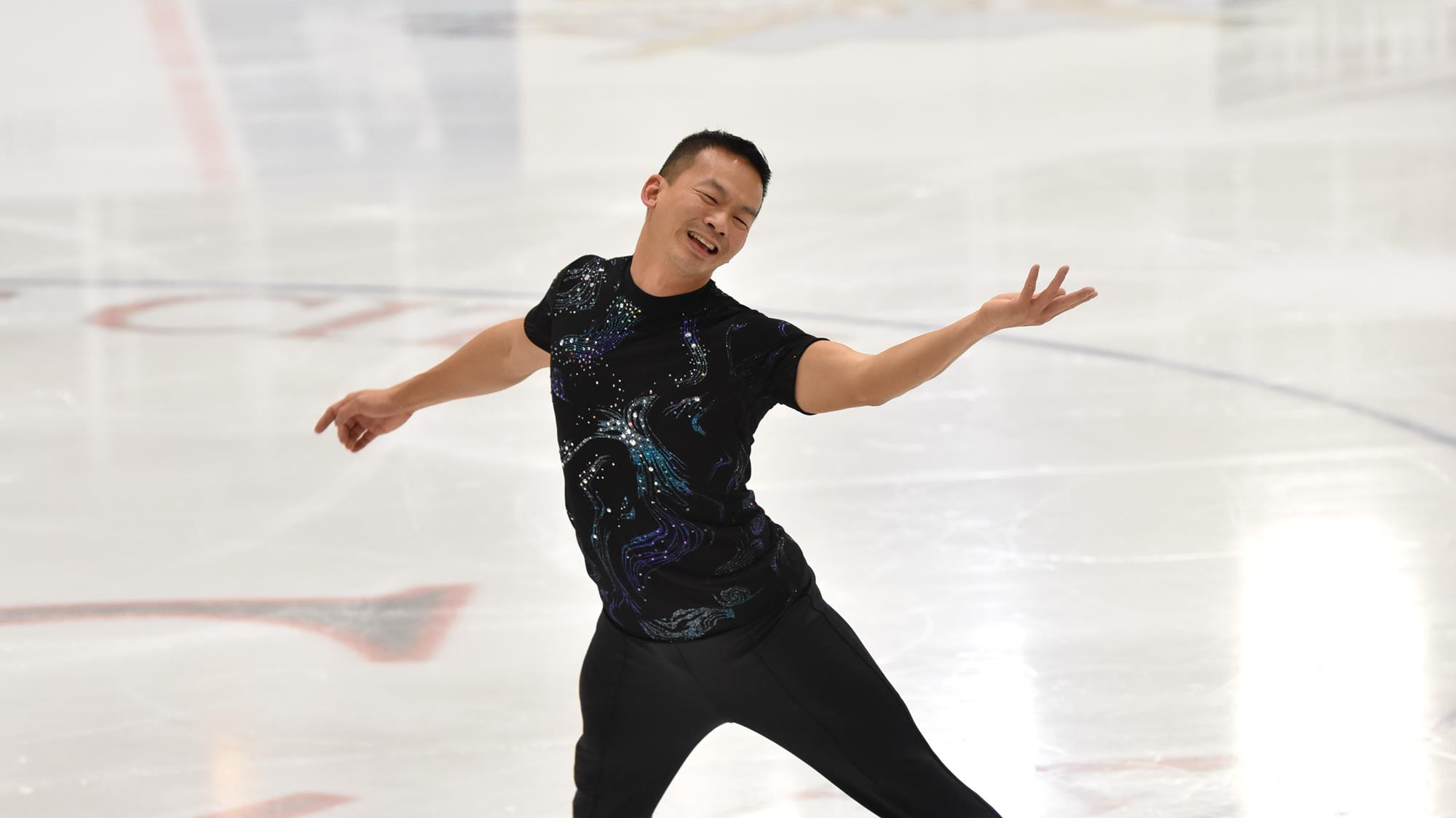 Ken Ho in a black costume performs a spread eagle with a big smile in 2019.