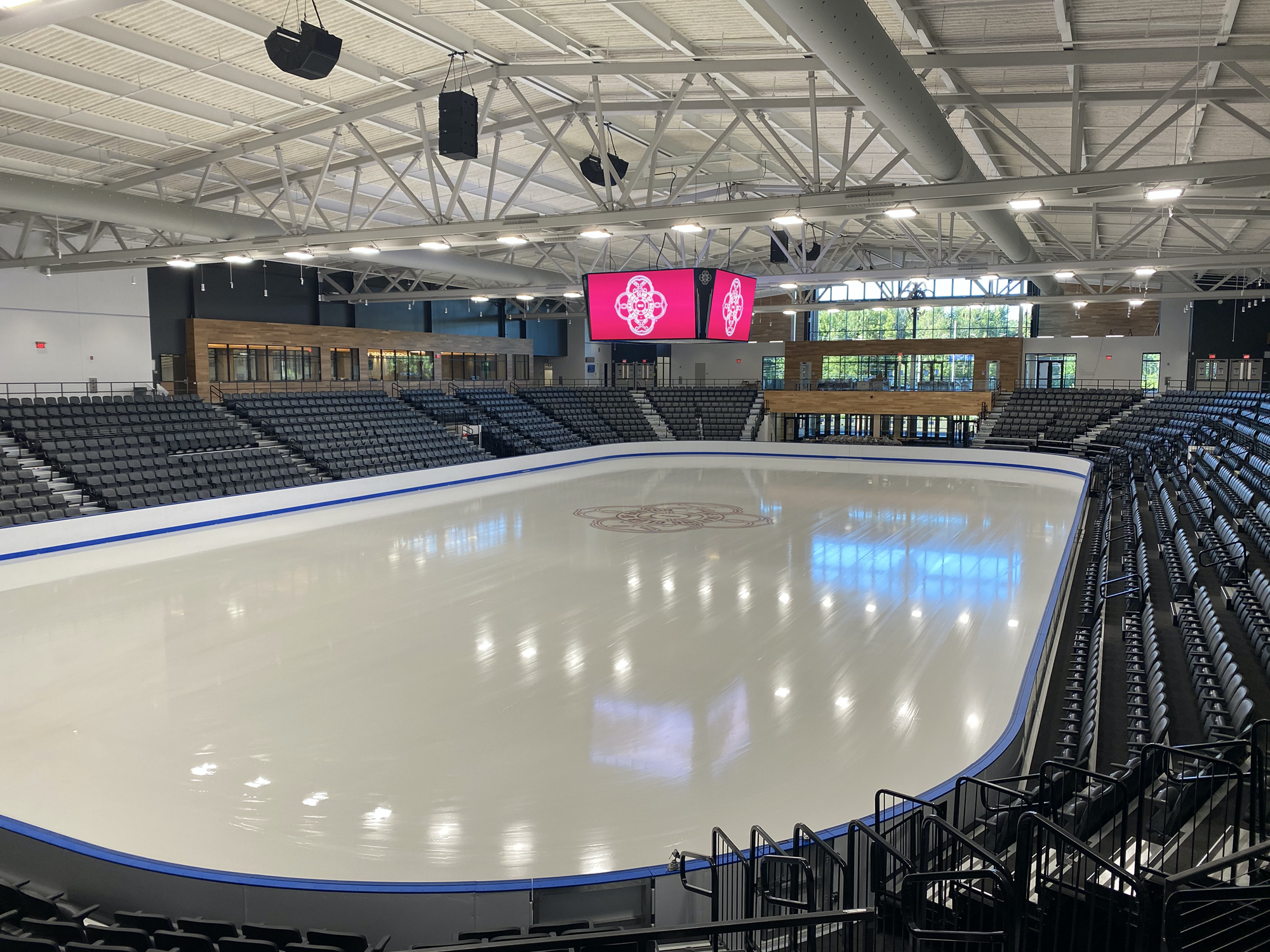 An ice rink surrounded by navy blue seats and a pink screen on a video board hanging overhead.