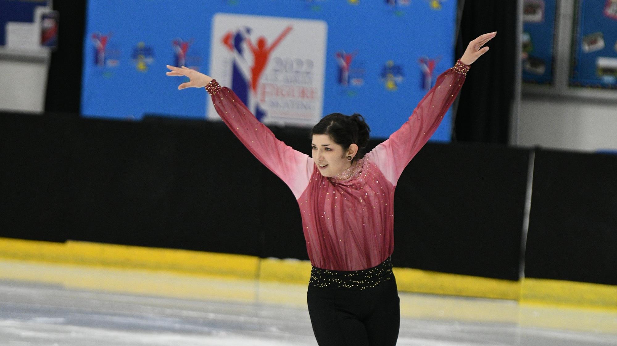 Niko Cohen in a pink and red costume and black pants on the ice.
