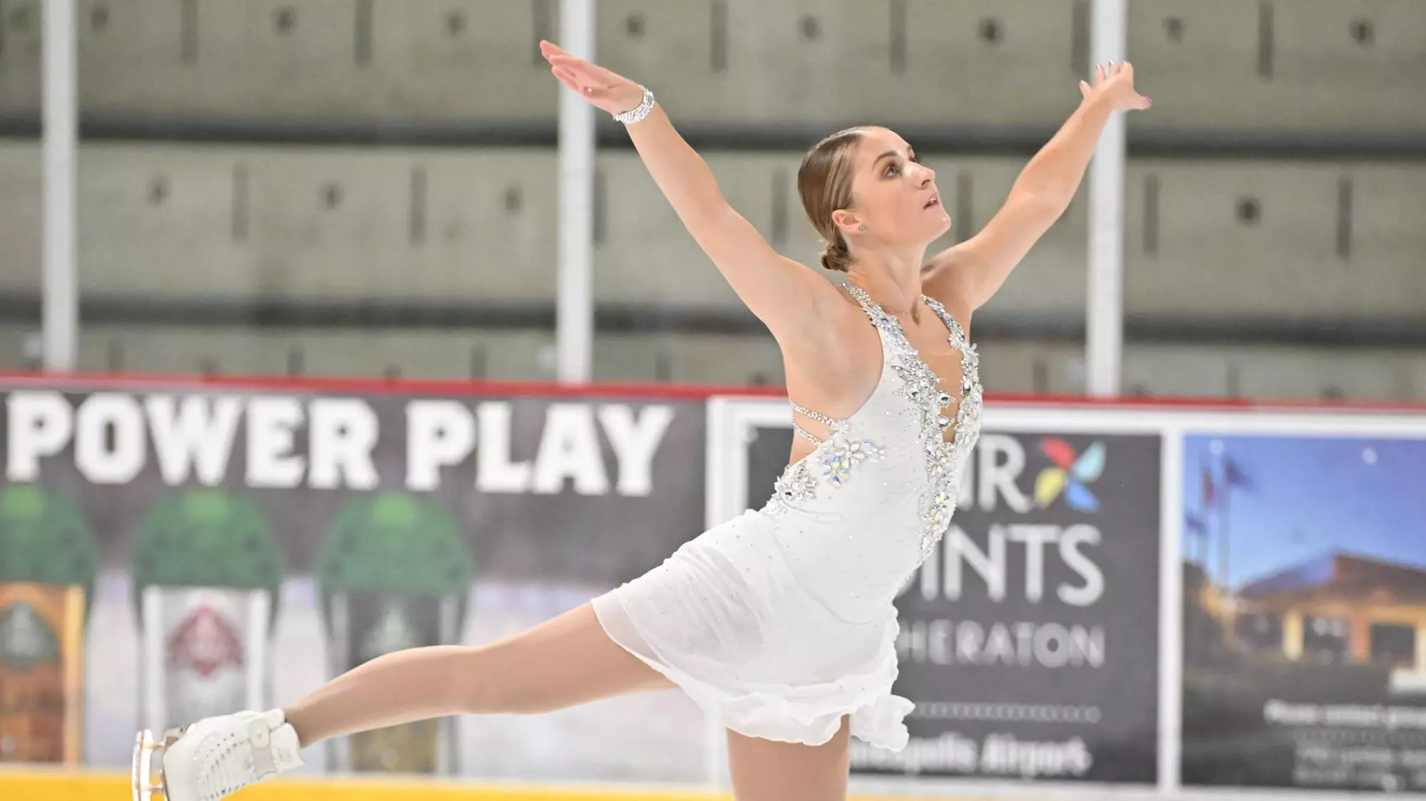 Paige Rydberg in all white spreads her arms up and leg behind her as she skates her free skate.