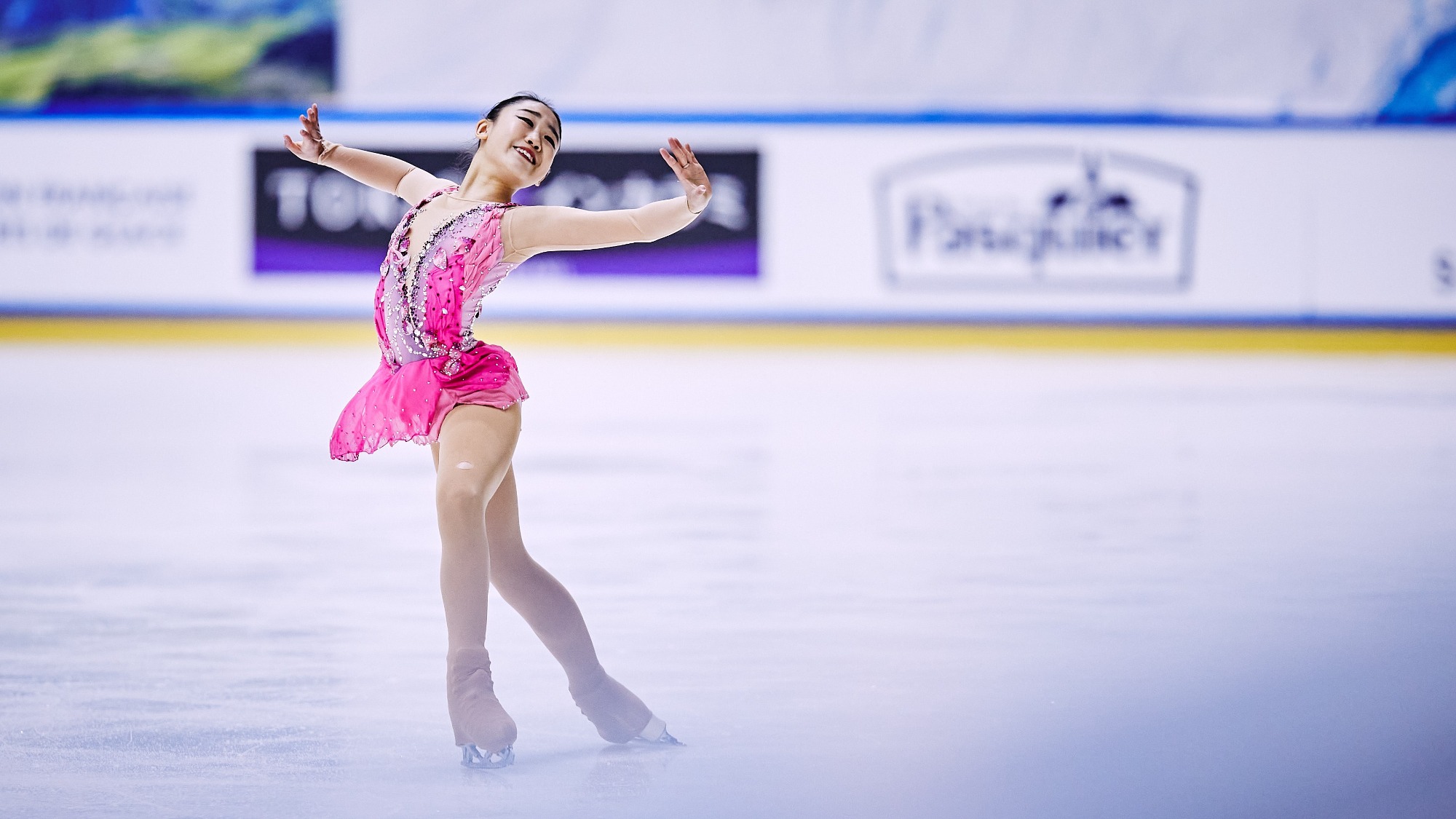 Clare Seo in a pink dress spreads her arms out wide and smiles on the ice at least year's Junior Grand Prix France.