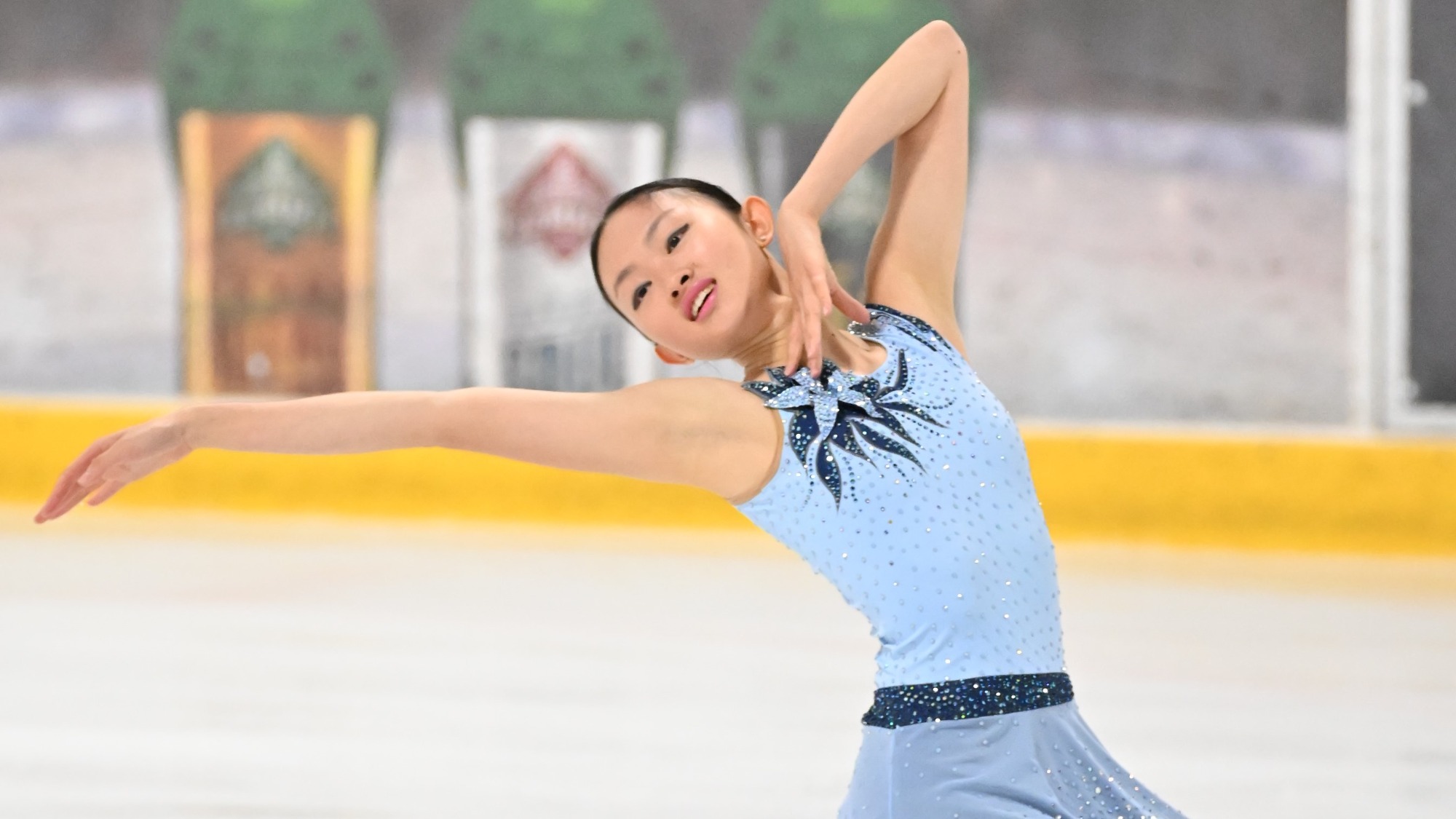 Audrey Lu, in a light blue and navy dress with a flower at the top, looks over her right shoulder with her right arm extended in a pose.