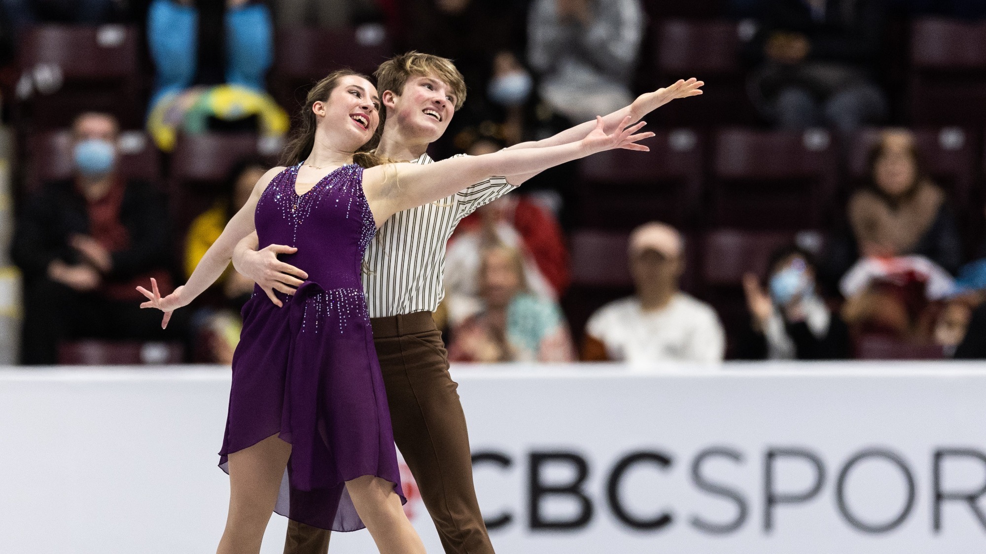 Emily Bratti and Ian Somerville smile as they hold their hand out and look over it at Skate Canada International. 