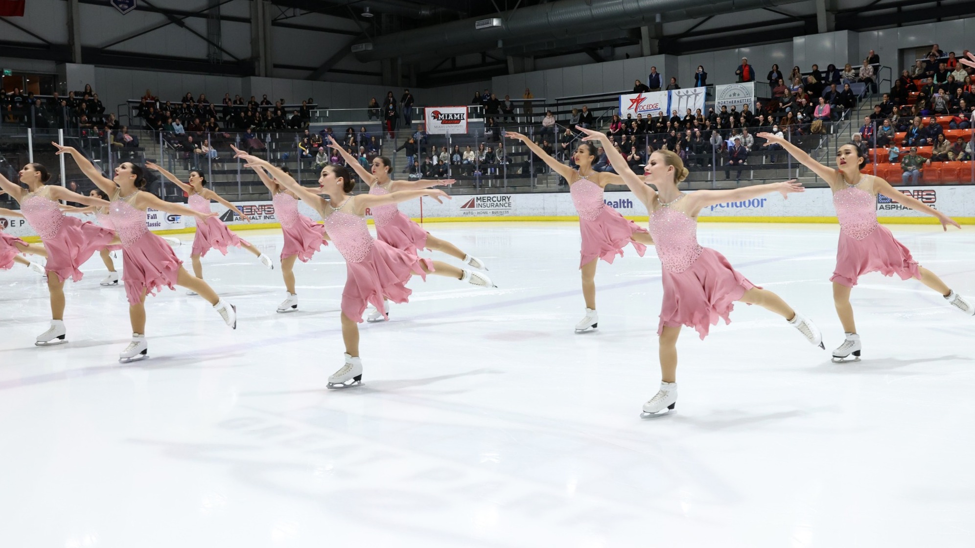 Skyliners Junior performs in baby pink dresses, reaching to their right.