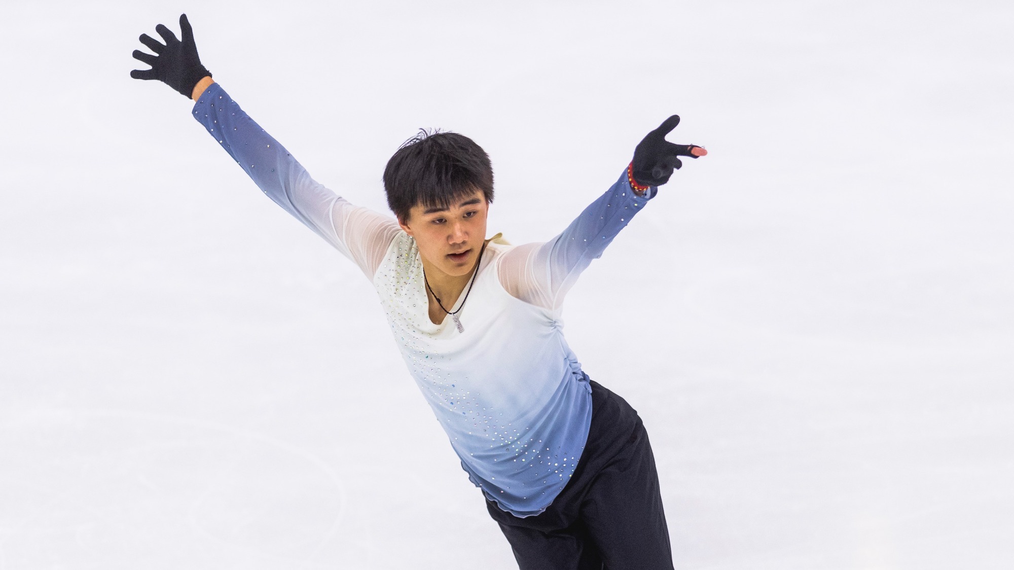 Michael Xie reaches up as he skates on the ice at a Junior Grand Prix early in the season.