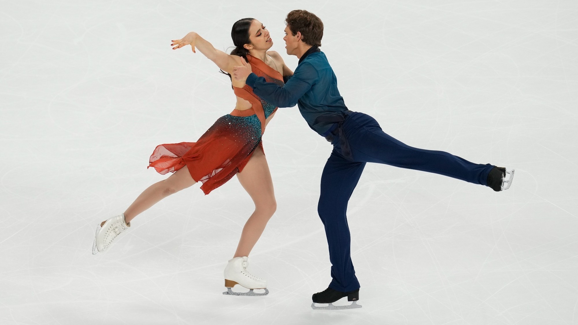 Caroline Green and Michael Parsons compete in th free dance at Cup of China 2023. Caroline (left) is wearing a green and orange skating costume with her long black hair tied back in a low ponytail. Michael is weating a green top with black pants. They face towards each other with one leg extended behind them. Caroline holds one arm up in the air. 