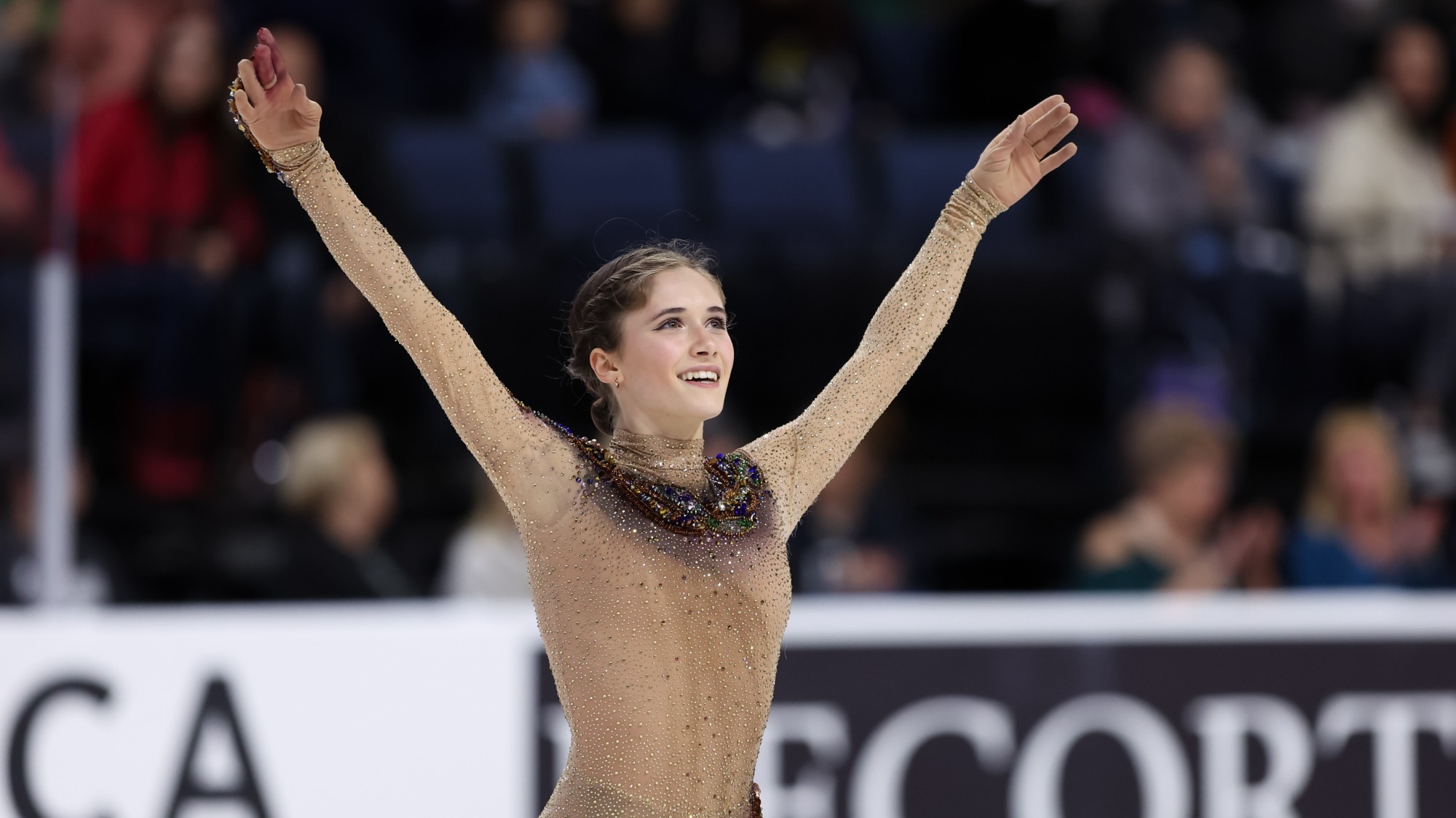 Isabeau Levito, wearing a light brown colored dress with a snake on it, raises her arms as she salutes the crowd.