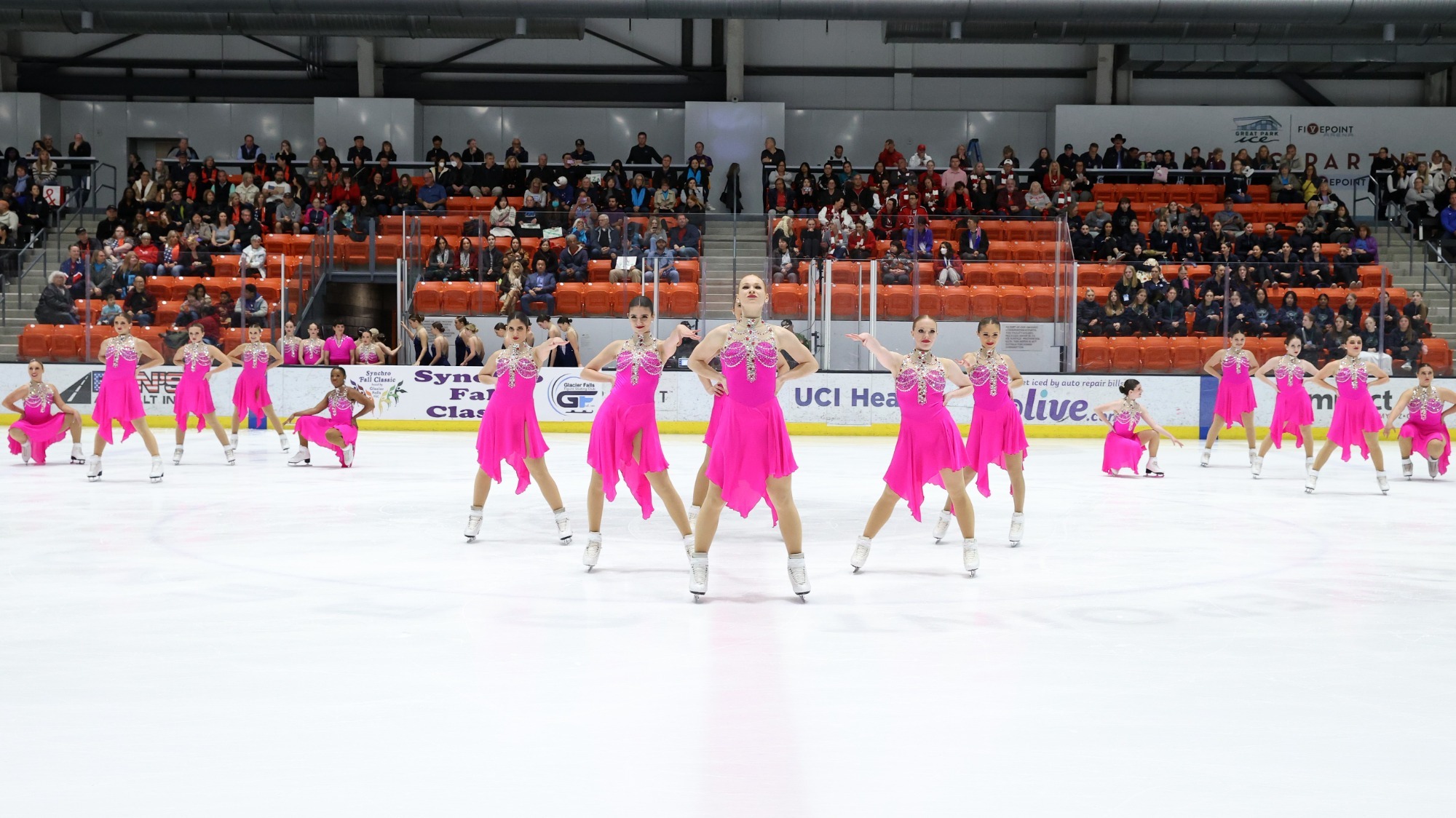 The Skyliners hit their final pose, in pink dresses. There are three blocks of girls, one center up front and two two the sides behind. All girls are standing except the two on the outsides in the two groups in the back. All have confident looks on their faces, standing in power poses.