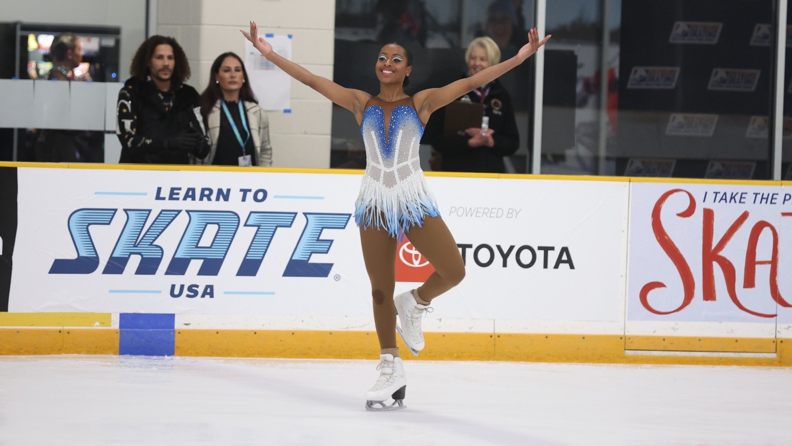 Alexa Gasparotto smiles, her arms up and out wide to present herself, as he skates onto the ice.