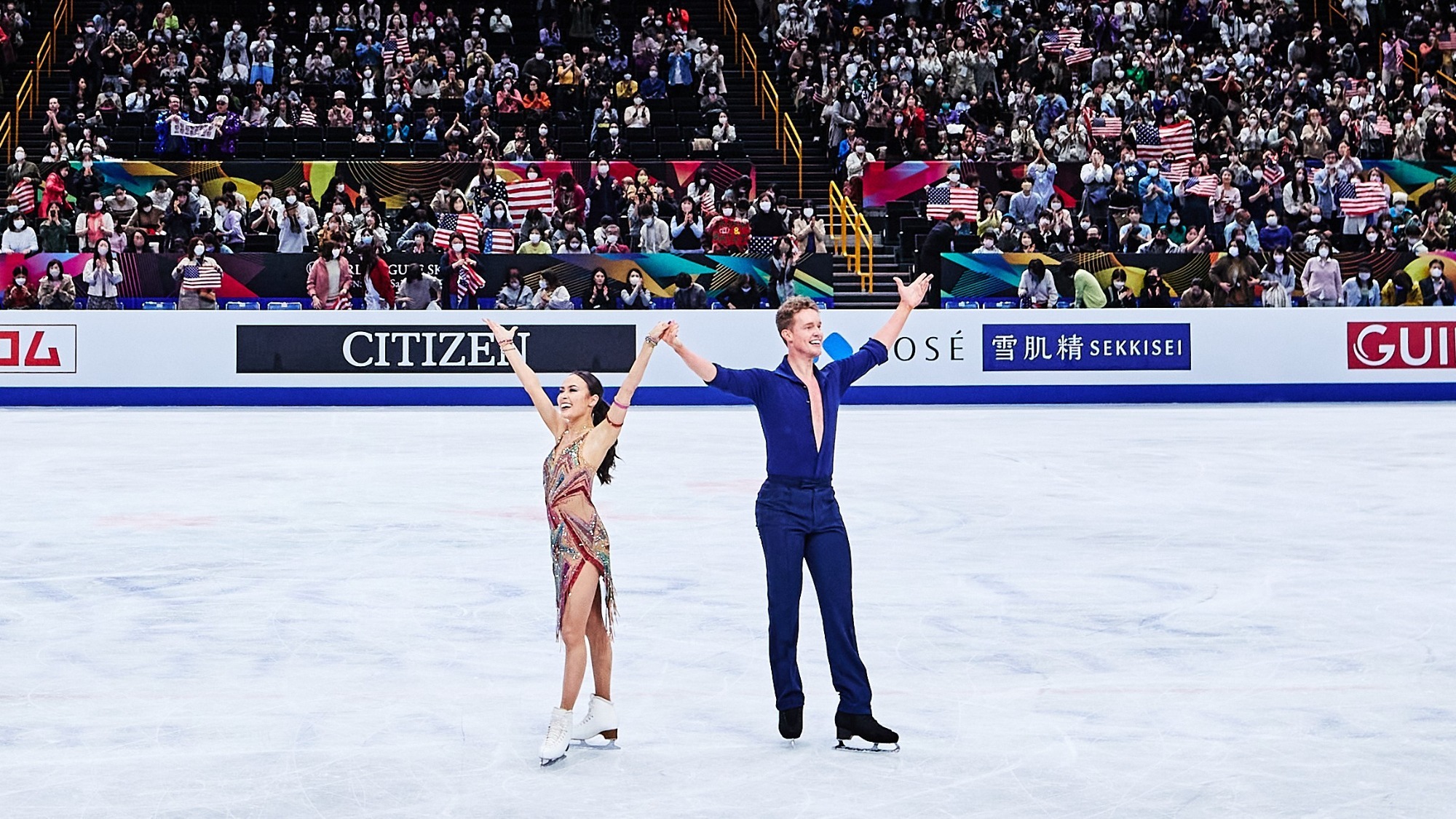 Taken as a wide shot with the crowd in the background, Madison Chock and Evan Bates salute the audience after the their rhythm dance at the ISU World Figure Skating Champinships 2023.
