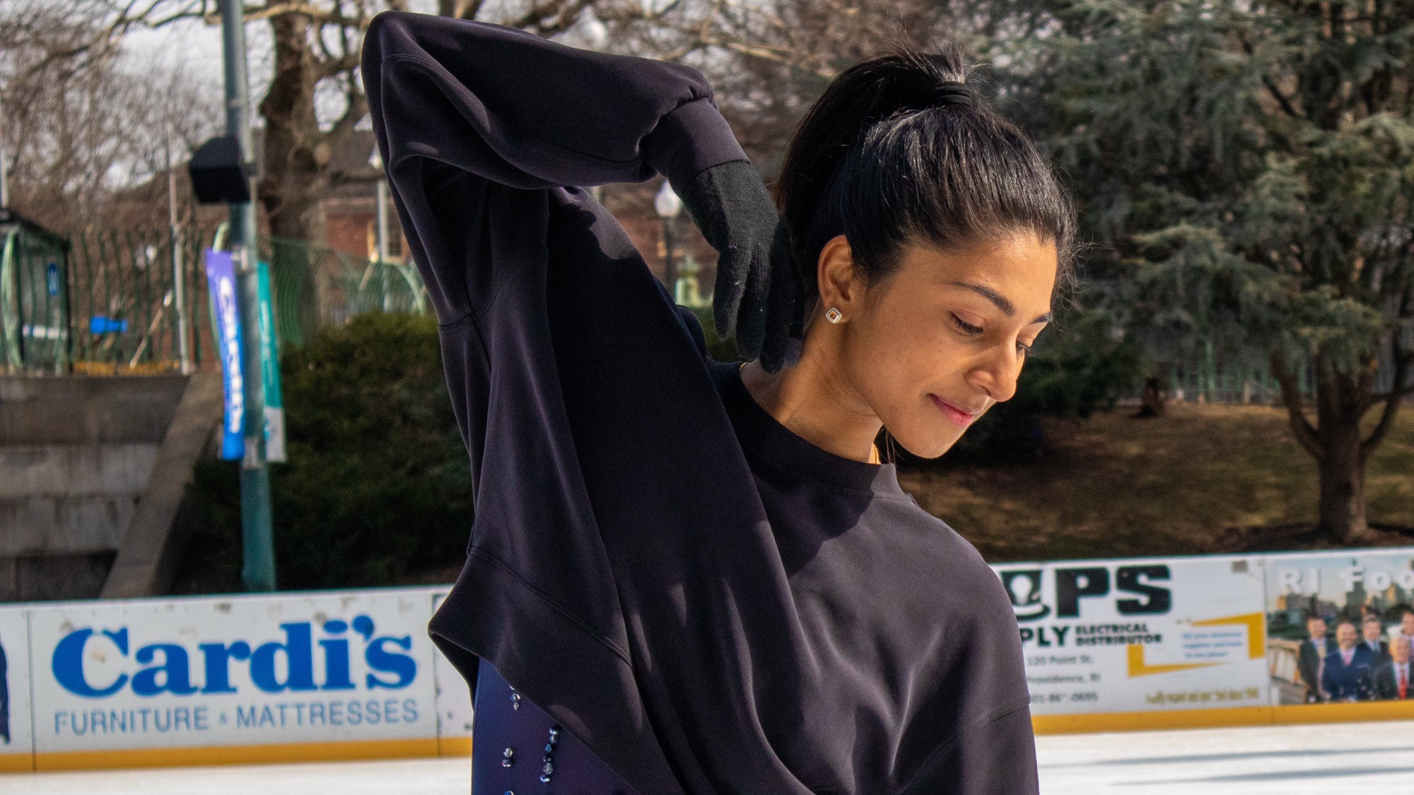 A closup of Pooja Kalyan. She is wearing a black crop sweatshirt and looks down to her right in a starting pose.