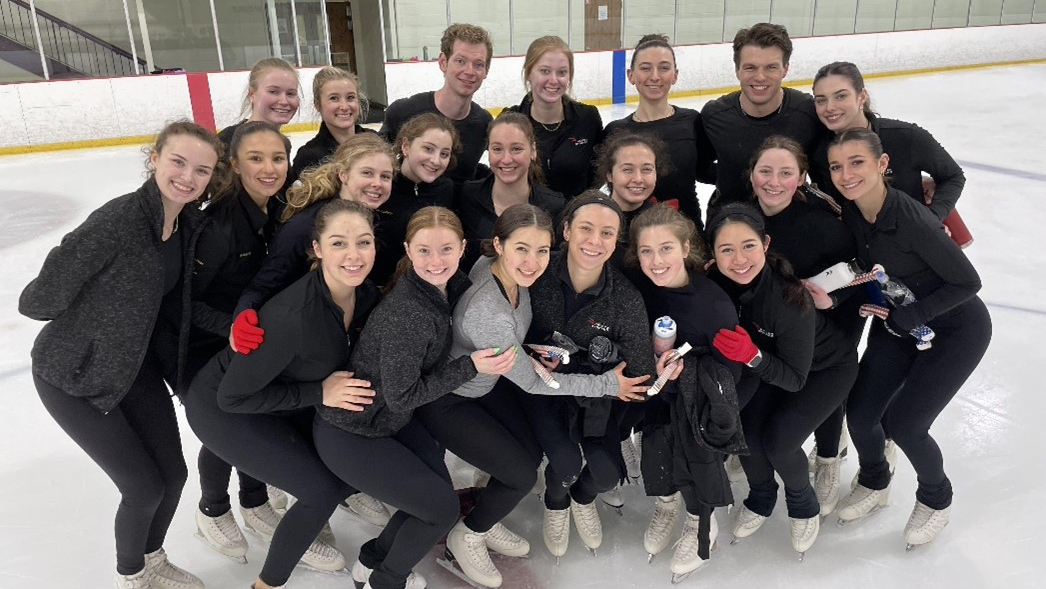 the 2022-23 Haydenettes, all dressed in black or grey, huddle together on the ice for a picture.