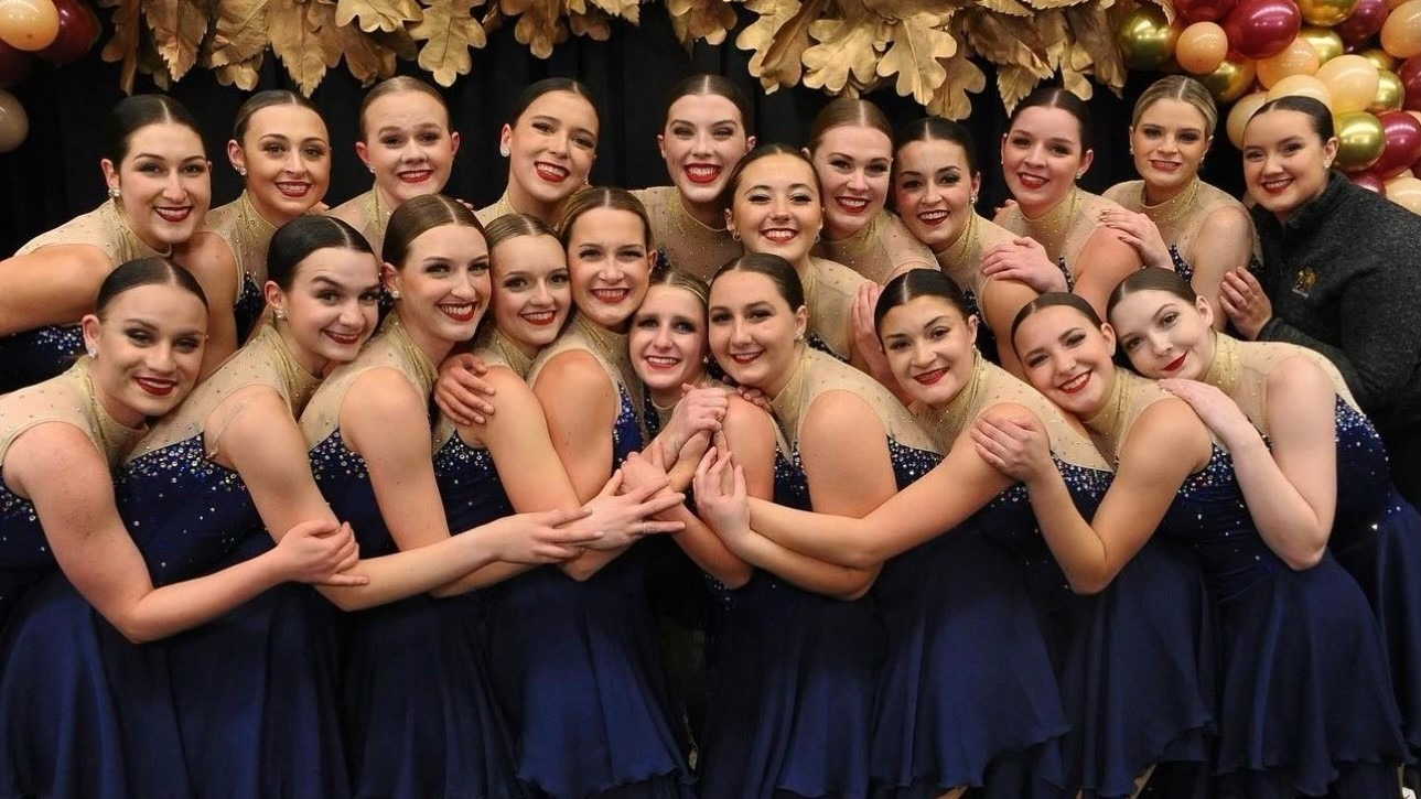 Adrian College, in blue and gold dresses, huddles close together to pose in the Kiss and Cry.