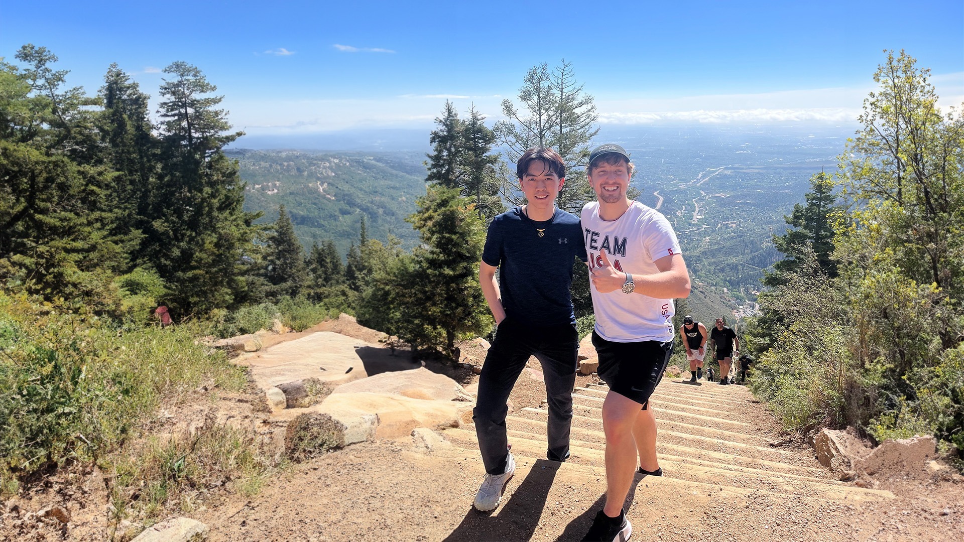  Vincent Zhou and Anthony Ponomarenko pose at the top of the Manitou Incline, Anthony holding a thumbs up. The rest of Colorado Springs can be seen below.