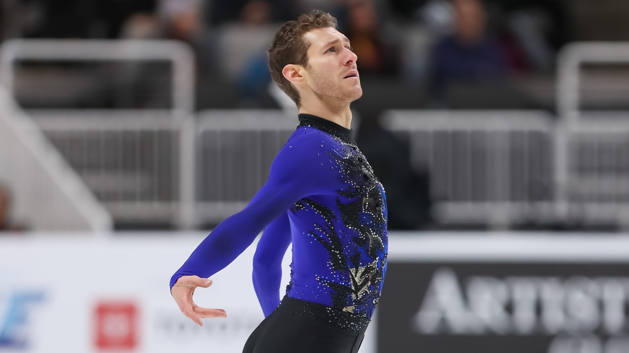 Jason Brown, dressed in a blue and black top, shown from the waist up, has his arms behind him, an emotional look on his face as he looks up while skating at last year's U.S. Championships.
