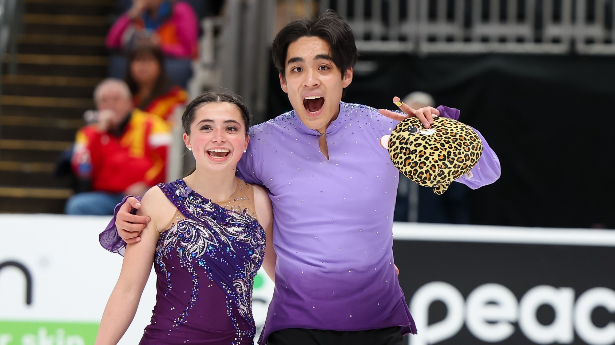 Taken from the waist up, Olivia Flores and Luke Wang look excited skating off the ice after their short program.
