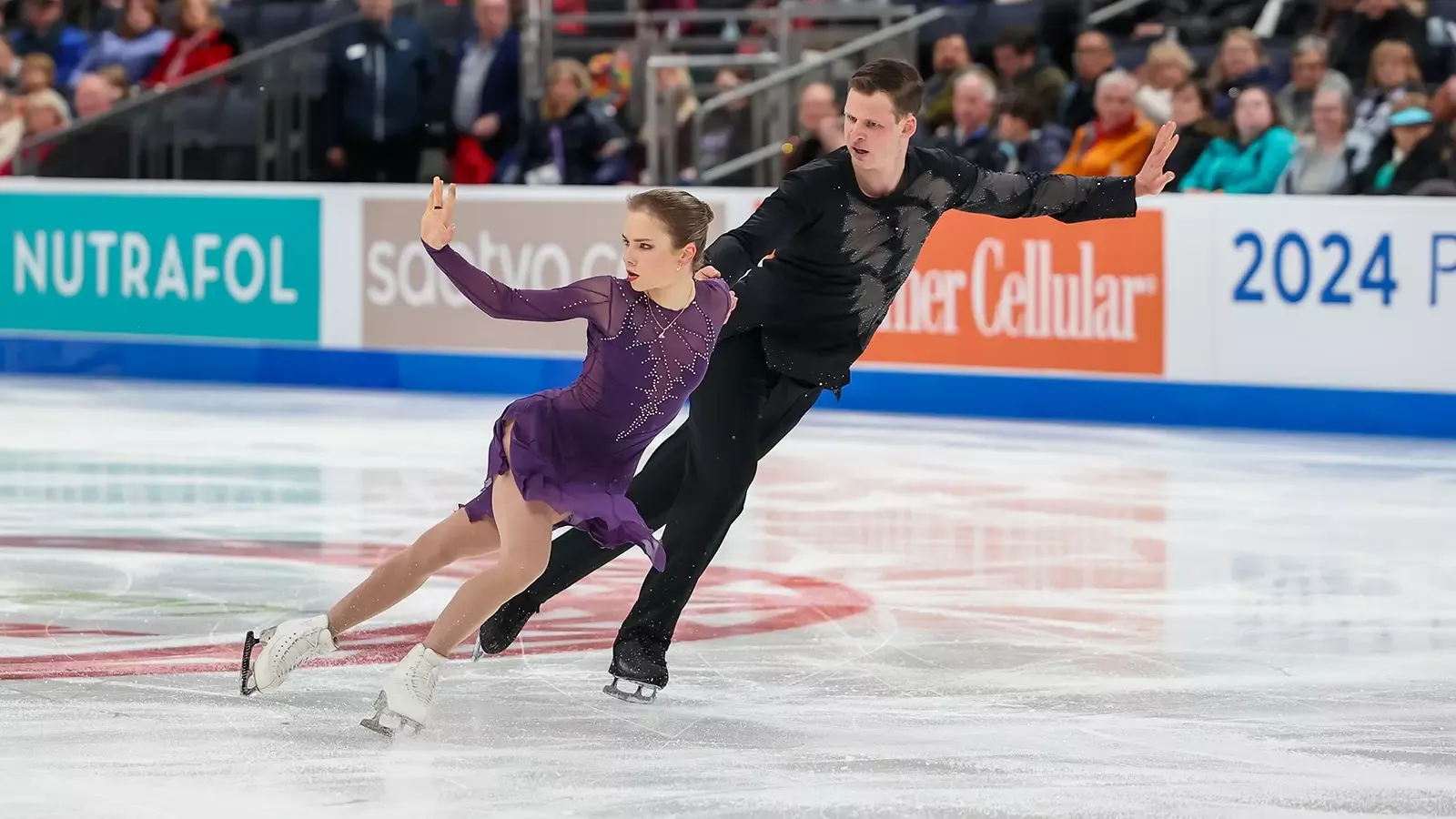 Dressed in purple, Alisa Efimova skates side by side with pairs partner Misha Mitrofanov, dressed in black.