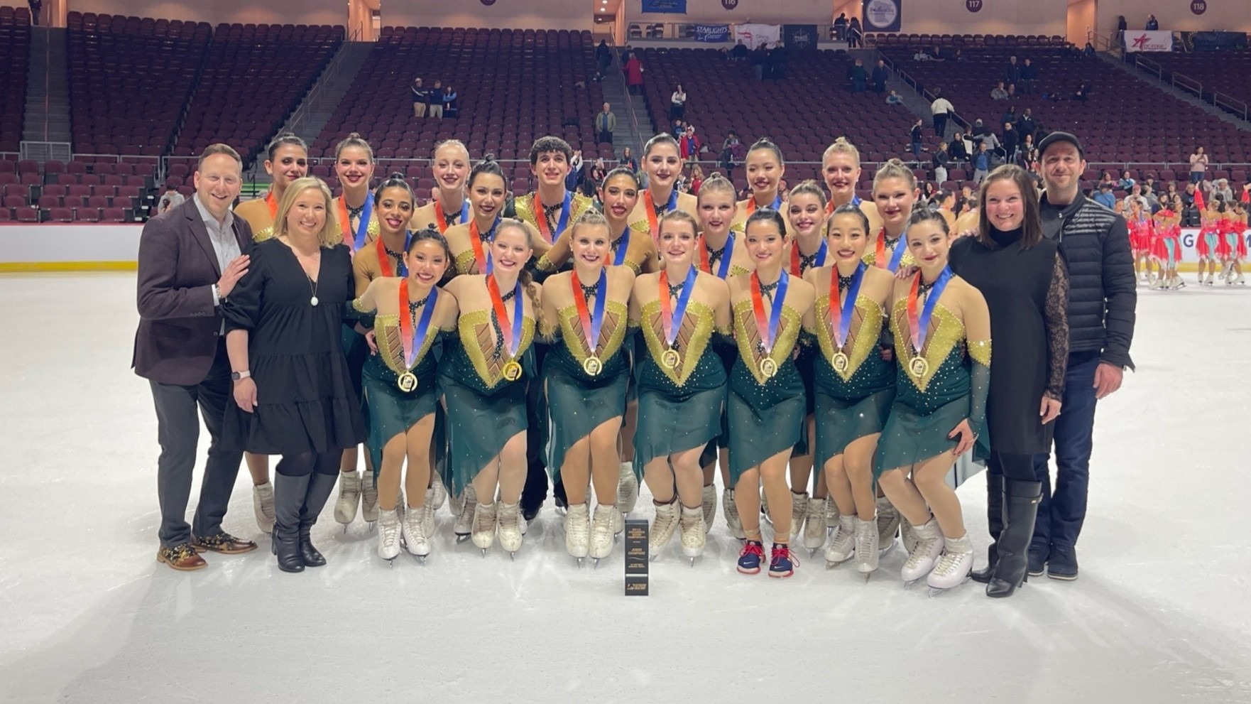 Group picture of Teams Elite wearing green and gold skating costumes with their gold medals. 