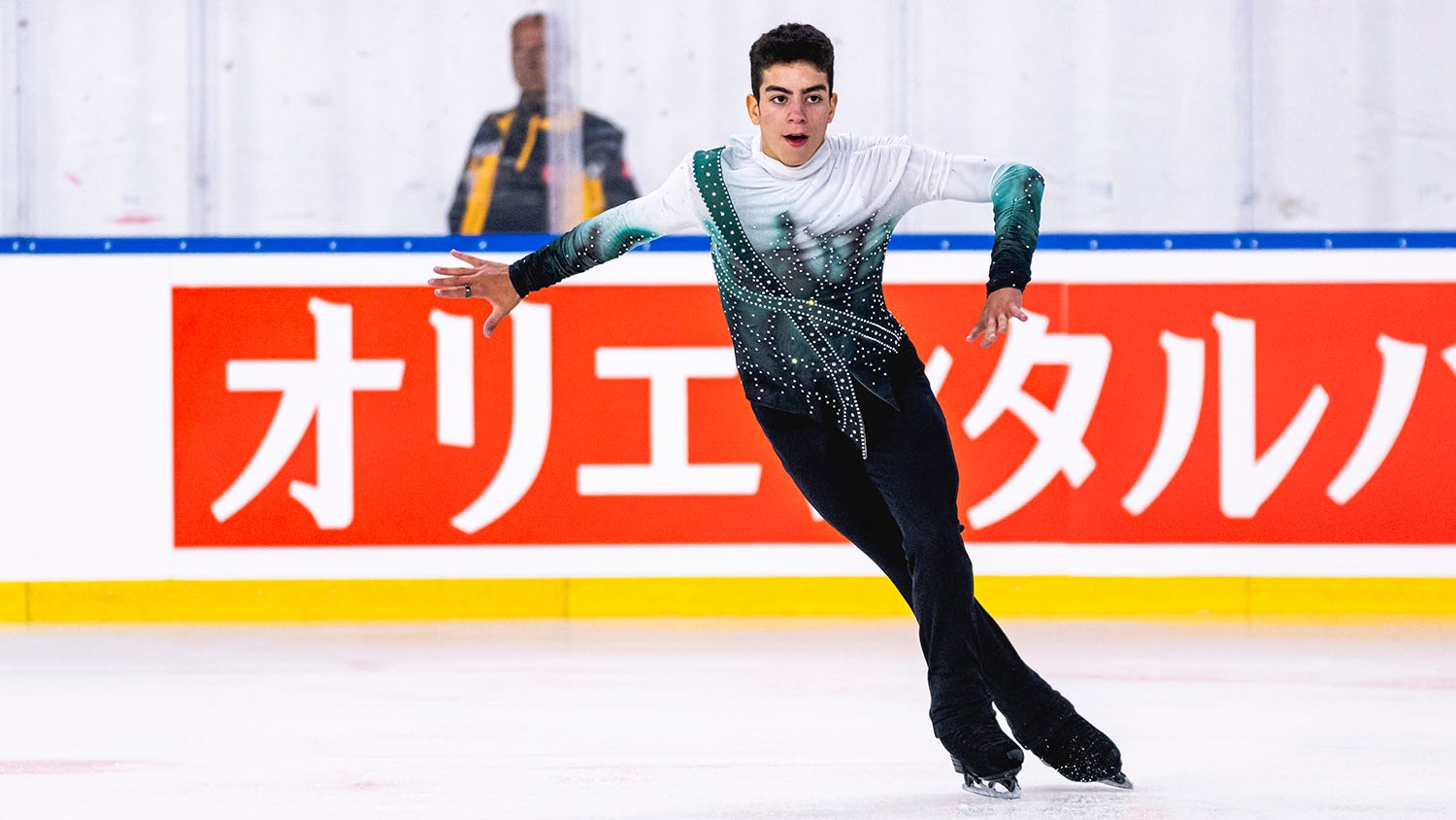 Jacob Sanchez skates forward his arms out to the side. He wears black pants and a white, green and black top.