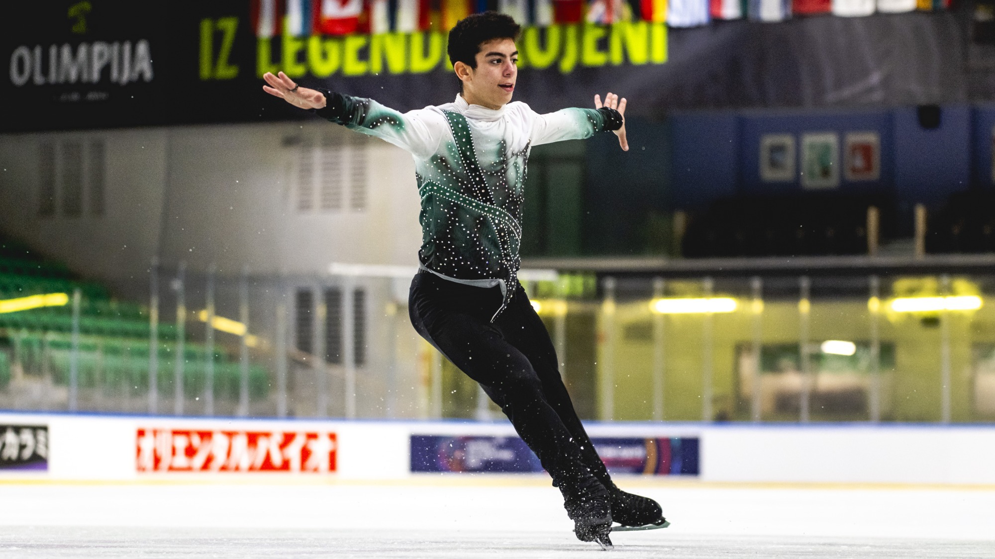 Jacob Sanchez completes a jump with his arms extended wearing a long sleeve white shirt with green and black details and black pants. 