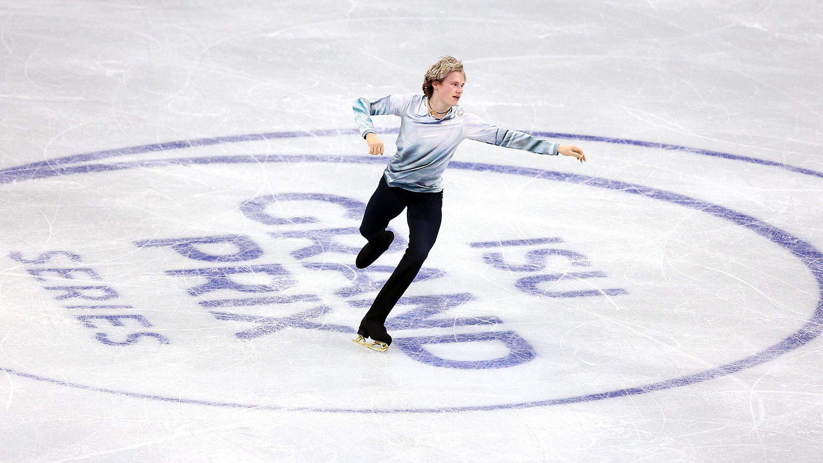 Dressed in a white top and black pants, World champion Ilia Malinin glides across the logo embedded in the ice at Skate Canada International. 