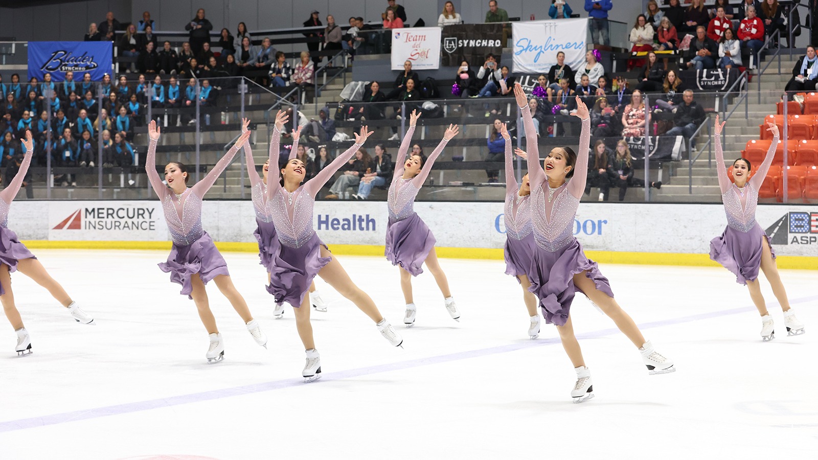 Skyliners junior all skates in their short program wearing matching purple long sleeve skating costumes. They all have their arms raised above their heads and are smiling. 