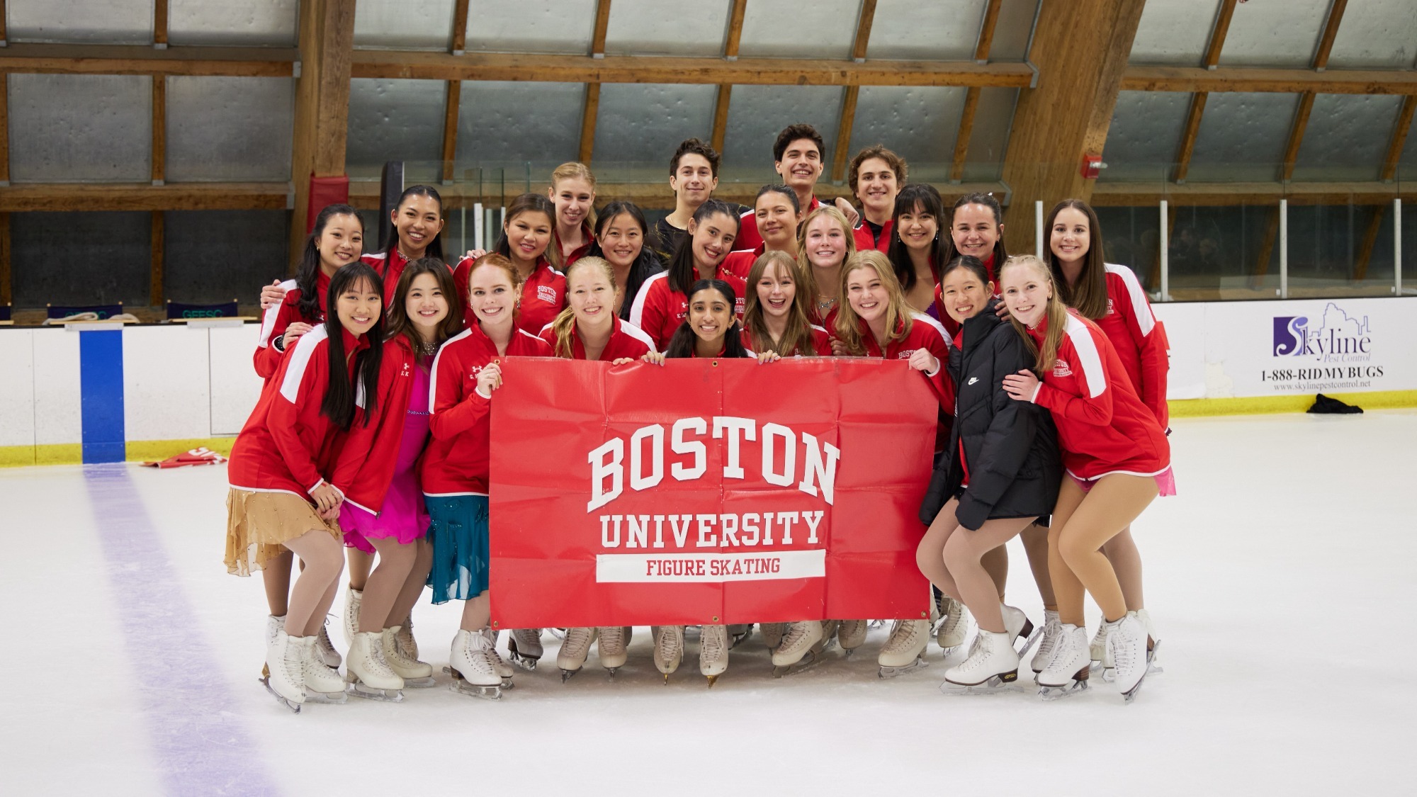 A group of skaters stand behind a red Boston University sign