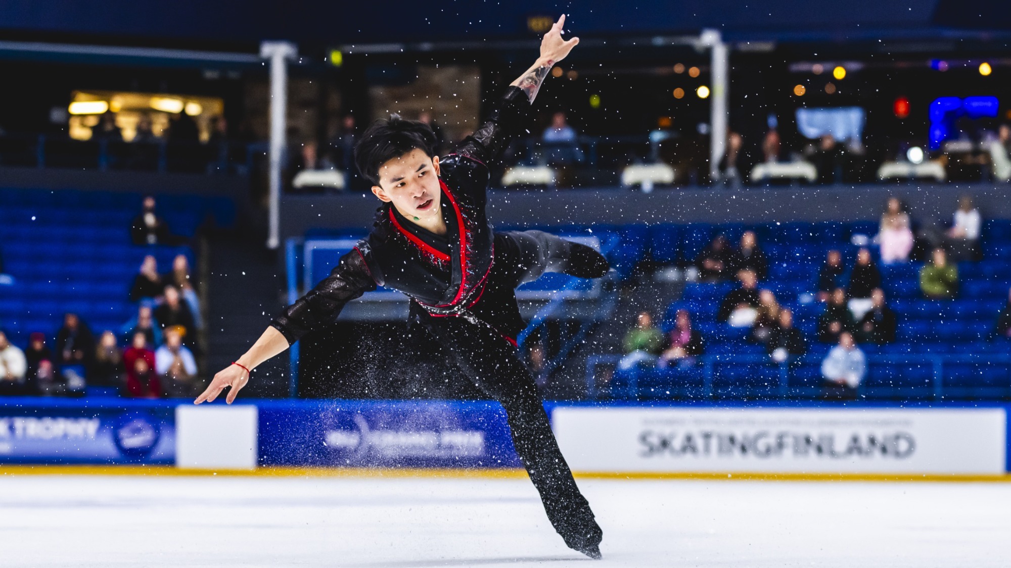 Jimmy Ma completes a jump with his arms and one leg outstretched. He is wearing a black top with red around the neckline. 