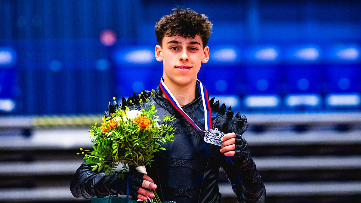 Patrick Blackwell poses on the podium holding his silver medal in one hand and a bouquet of flowers in the other. 