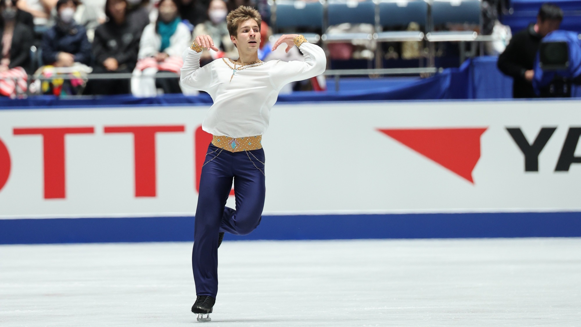 Wearing a white top, a tan waistband and blue pants, Andrew Torgashev dazzles the audience with this captivating footwork.