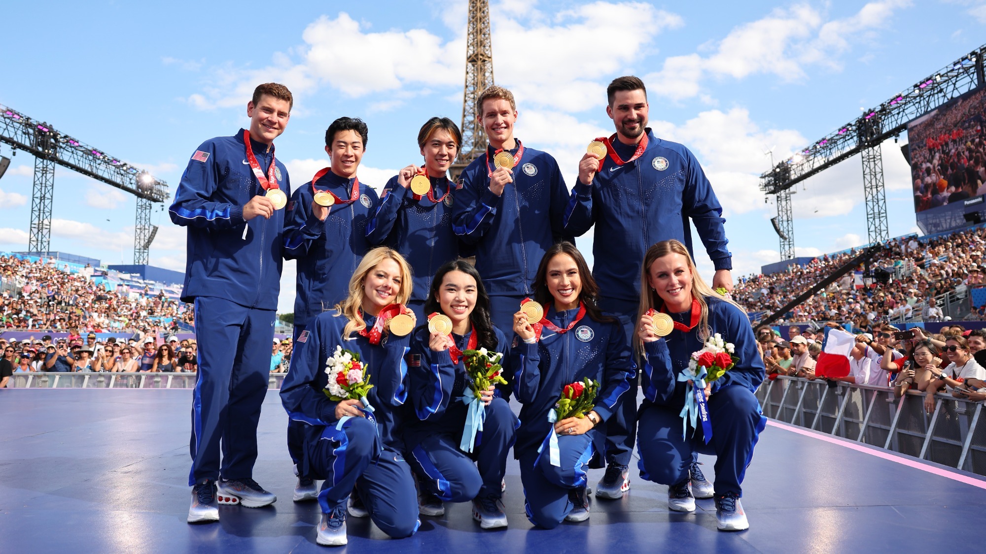The nine members of the Team USA figure skating team event pose in front of the Eiffel Tower holding their new gold medals from the 2022 Olympic Winter Games. 