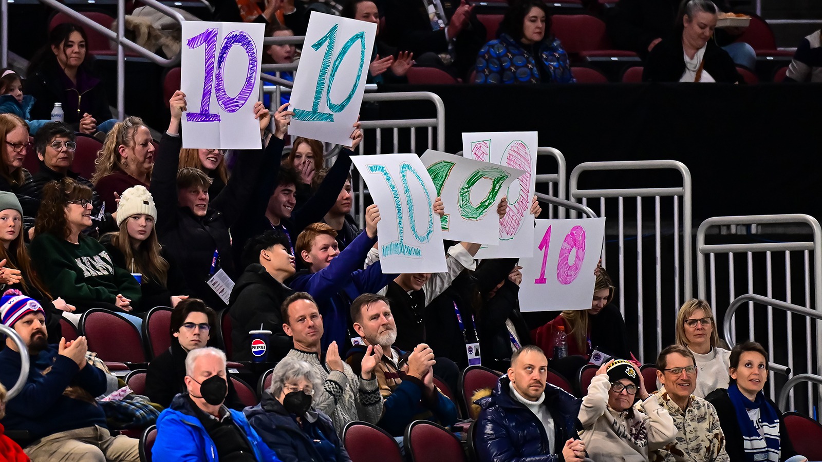 Crowd cheering in the stands at the 2025 Prevagen U.S. Figure Skating Championships. A few fans are holding signs with big a big 