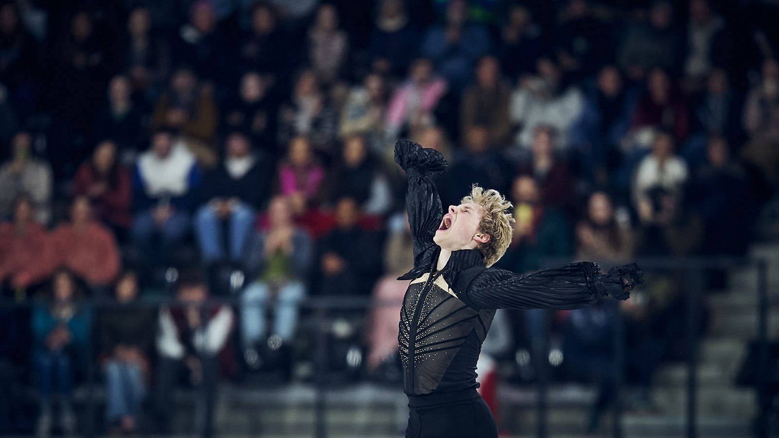 Ilia Malinin, wearing black, throws his arms up in the air in celebration of his winning free skate at Grand Prix de France.