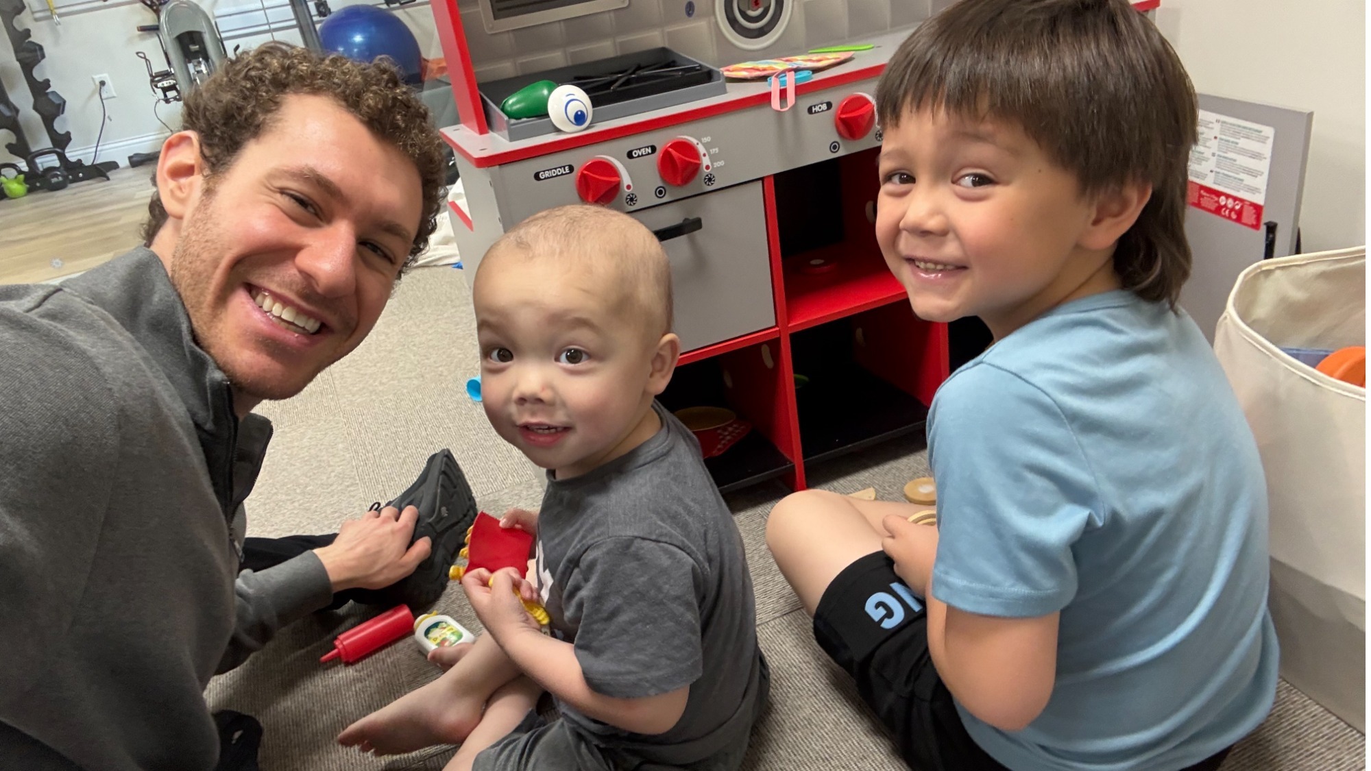A smiling Jason Brown sits on the floor and plays with children staying at the Ronald McDonald House. 