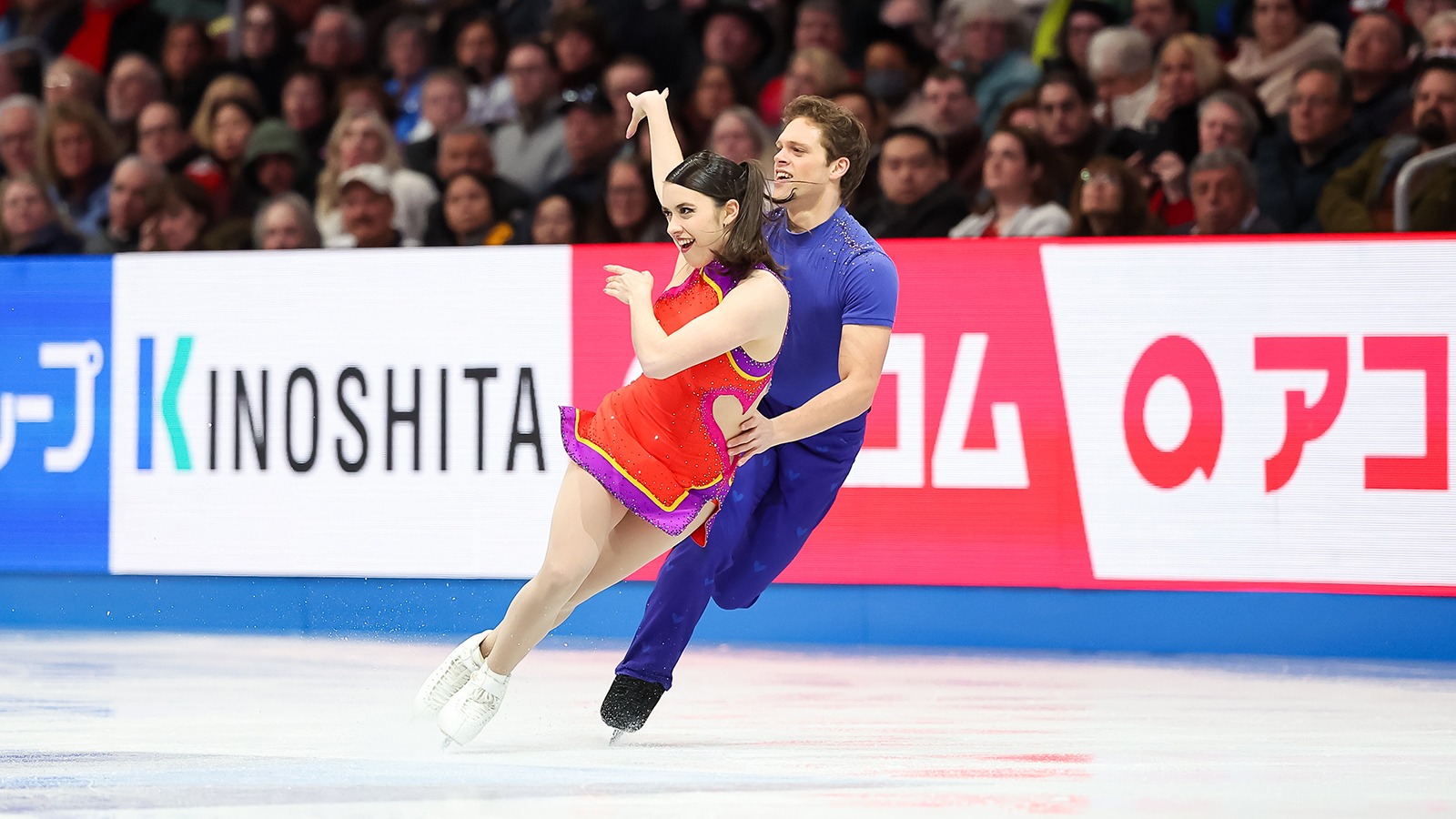 Caroline Green, dressed in red, and Michael Parsons, dressed in blue, skate side by side at the 2025 World Championships.