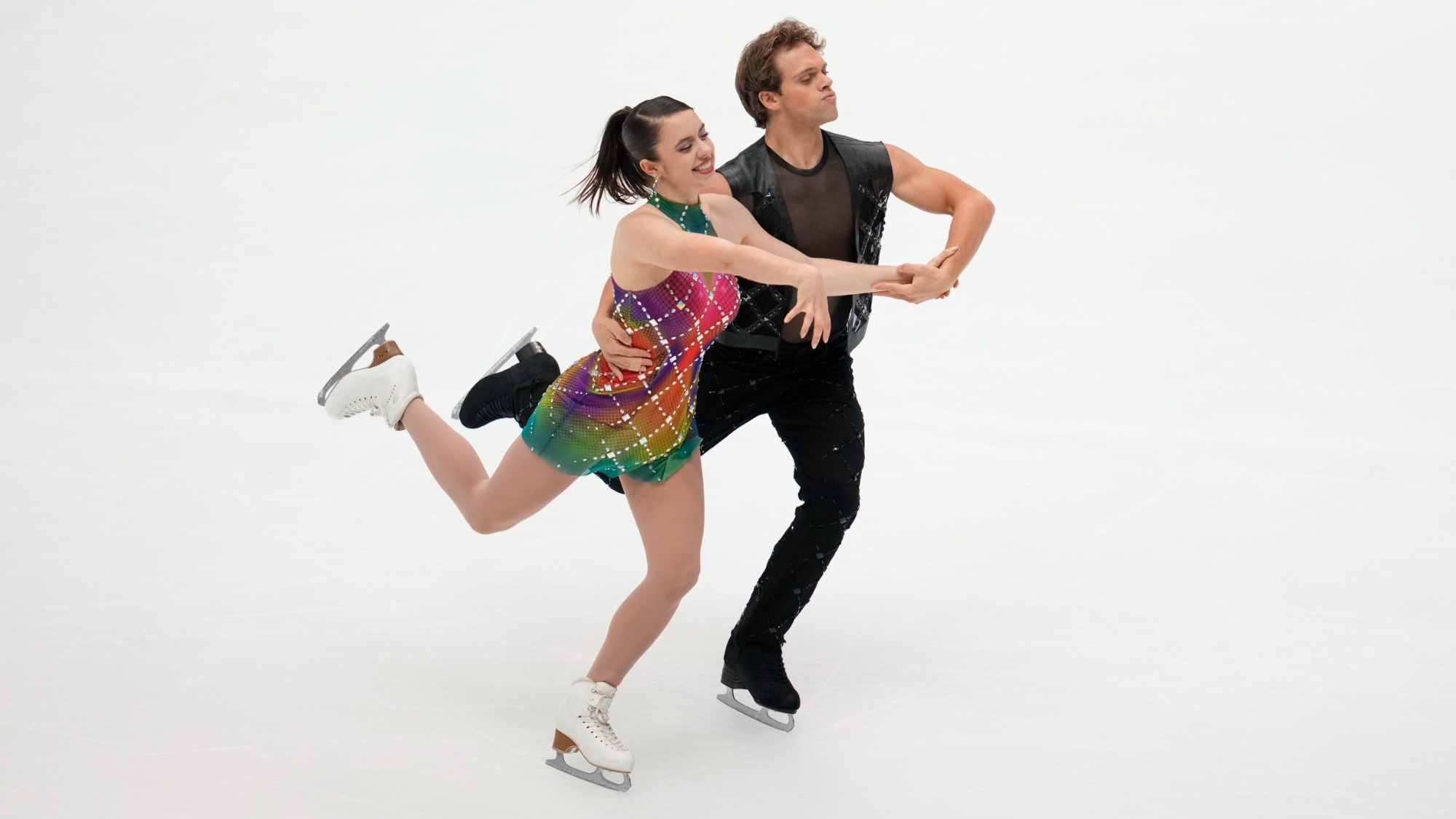 Caroline Green and Michael Parsons skate in hold at NHK Trophy. She wears a rainbow colored dress, while he wears all black.