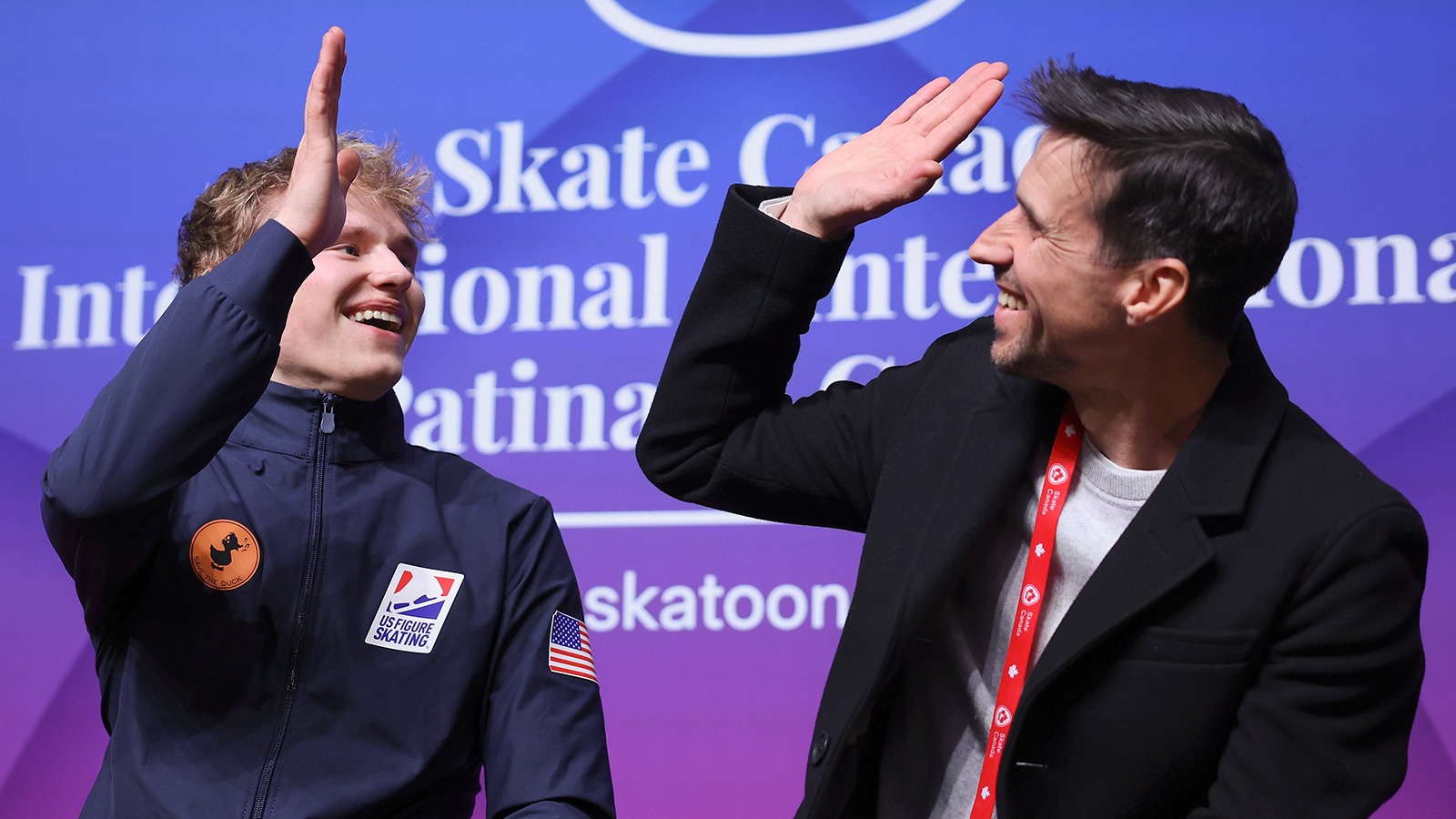 Ilia Malinin and his coach and father high-five each other in the kiss and cry at Skate Canada International. 