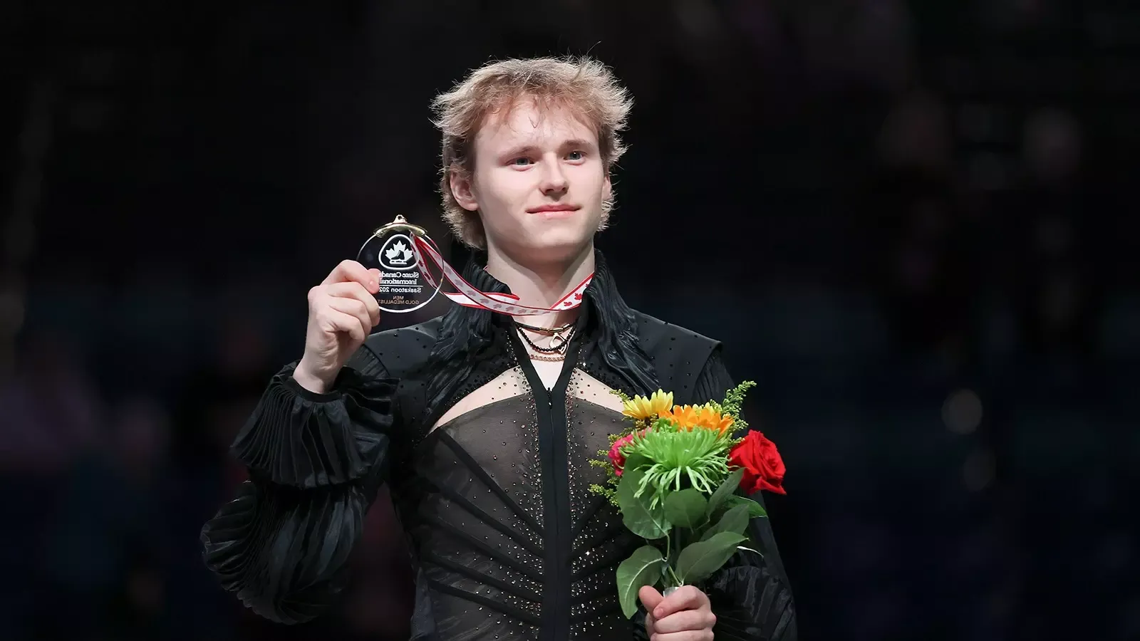 Ilia Malinin holds up a gold medal and flowers after a victory this season on the Grand Prix Series