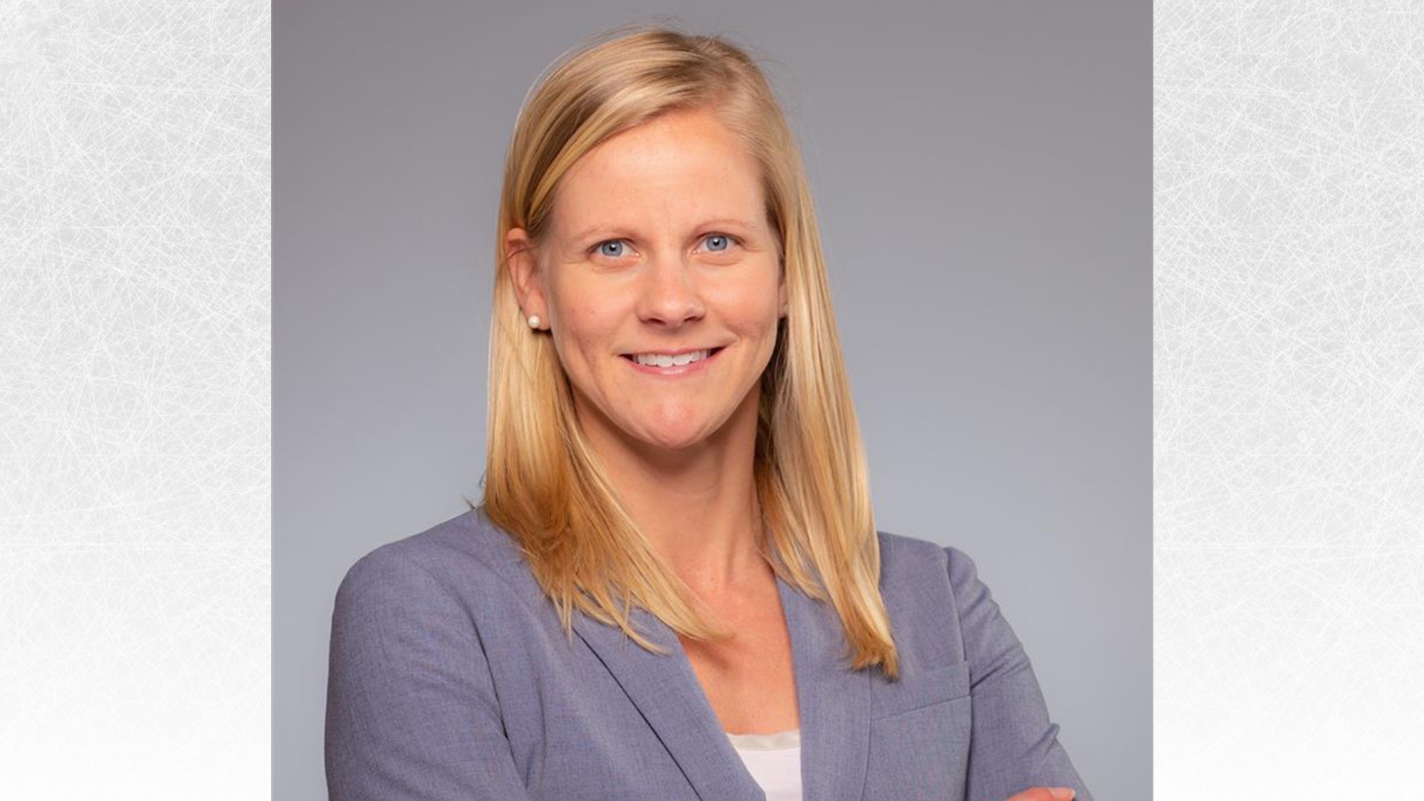 Photo of Heather Palmer taken from the waist up. She stands with her arms crossed and a smile on her face. Heather is a woman with shoulder length blonde hair wearing a grey blazer over a white top and pearl earrings