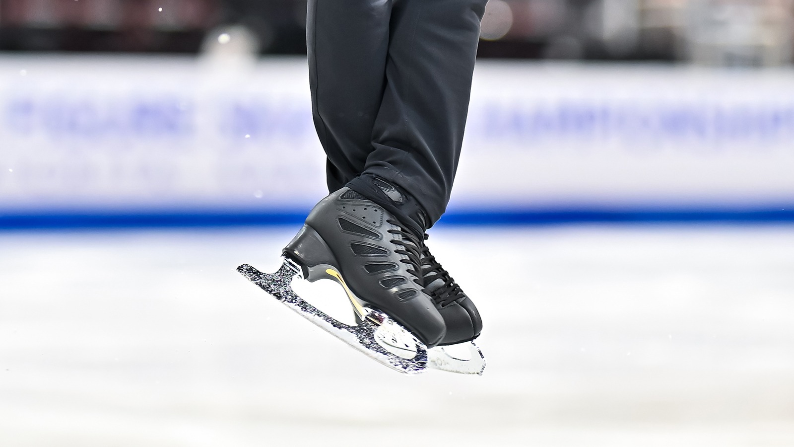 Closeup of a pair of black skates. The skater is wearing black pants