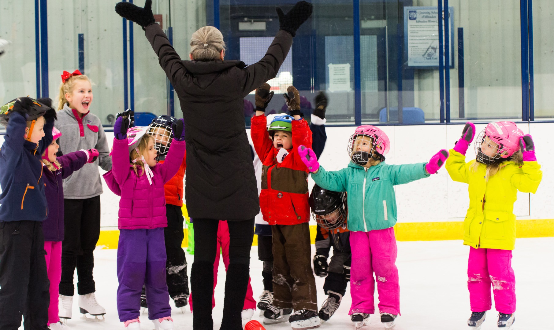Several young skaters give a big smile with their arms up on the ice