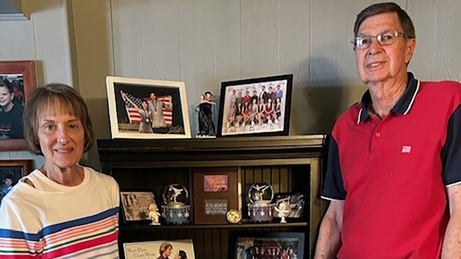 Janice and Terry Collins stand in front of a book shelf full of pictures from the U.S. National Team.