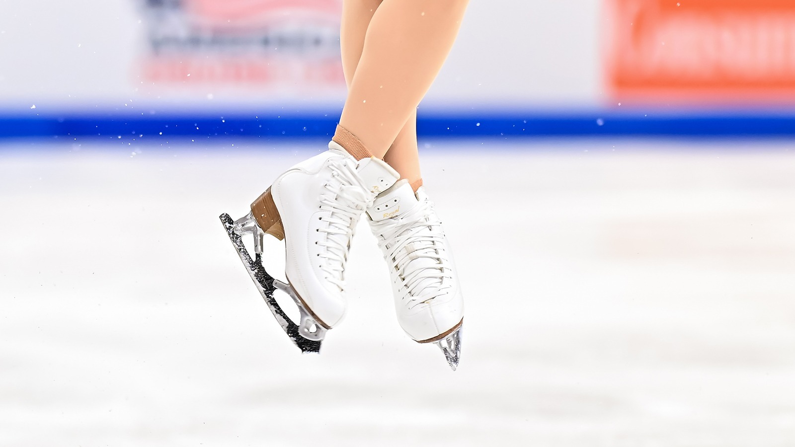 Close up photo of a pair of white figure skates as an athlete performs a jump