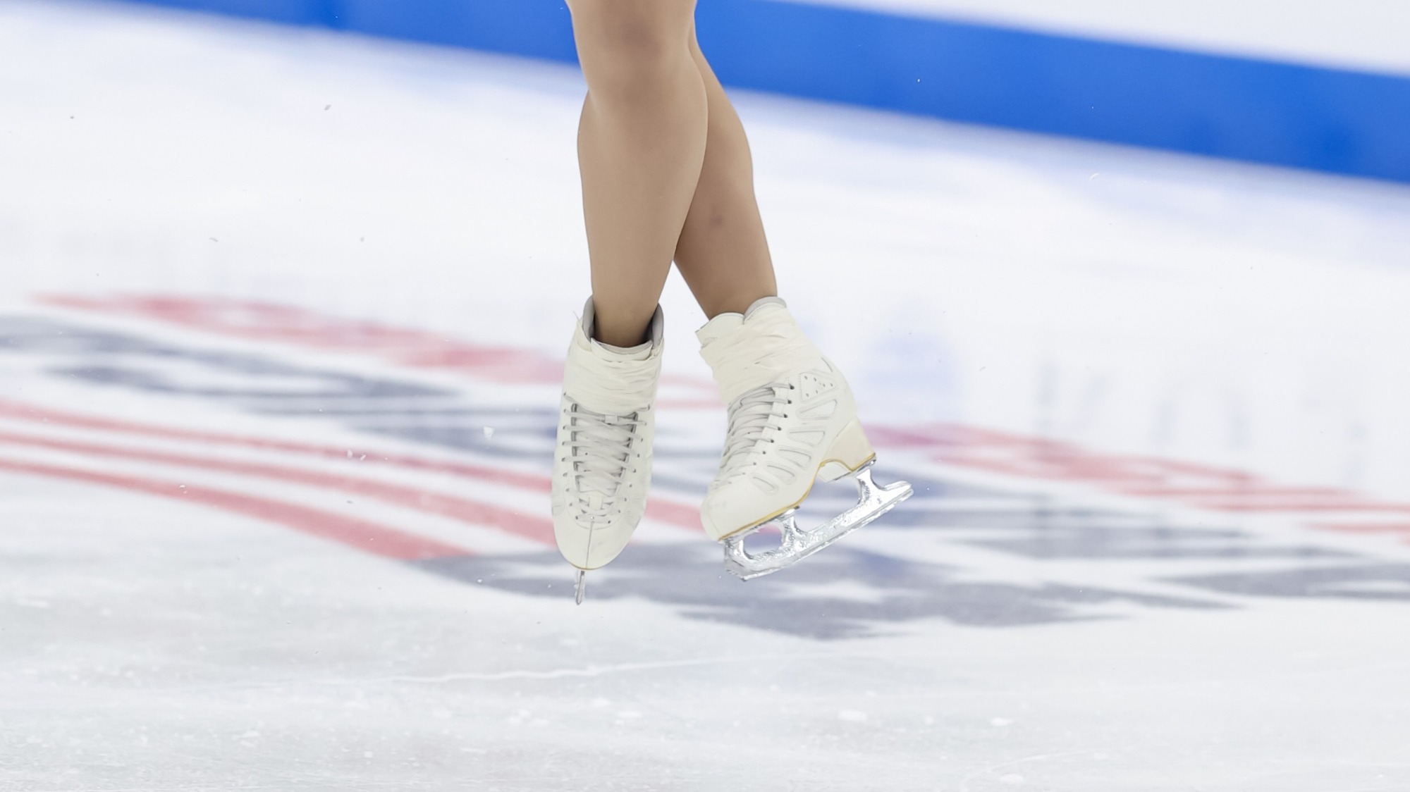 Close of a female athlete's white skates with one leg crossed over the other