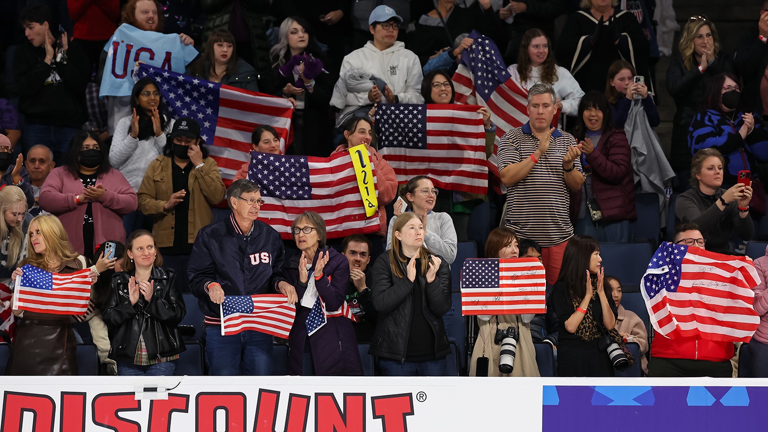 Fans give a standing ovation and wave American flags while clapping and cheering.