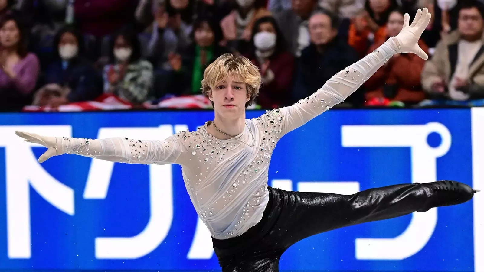 Lucius Kazanecki, dressed in white top, lands a jump with arms extended during his short program at the Junior Grand Prix Final. 