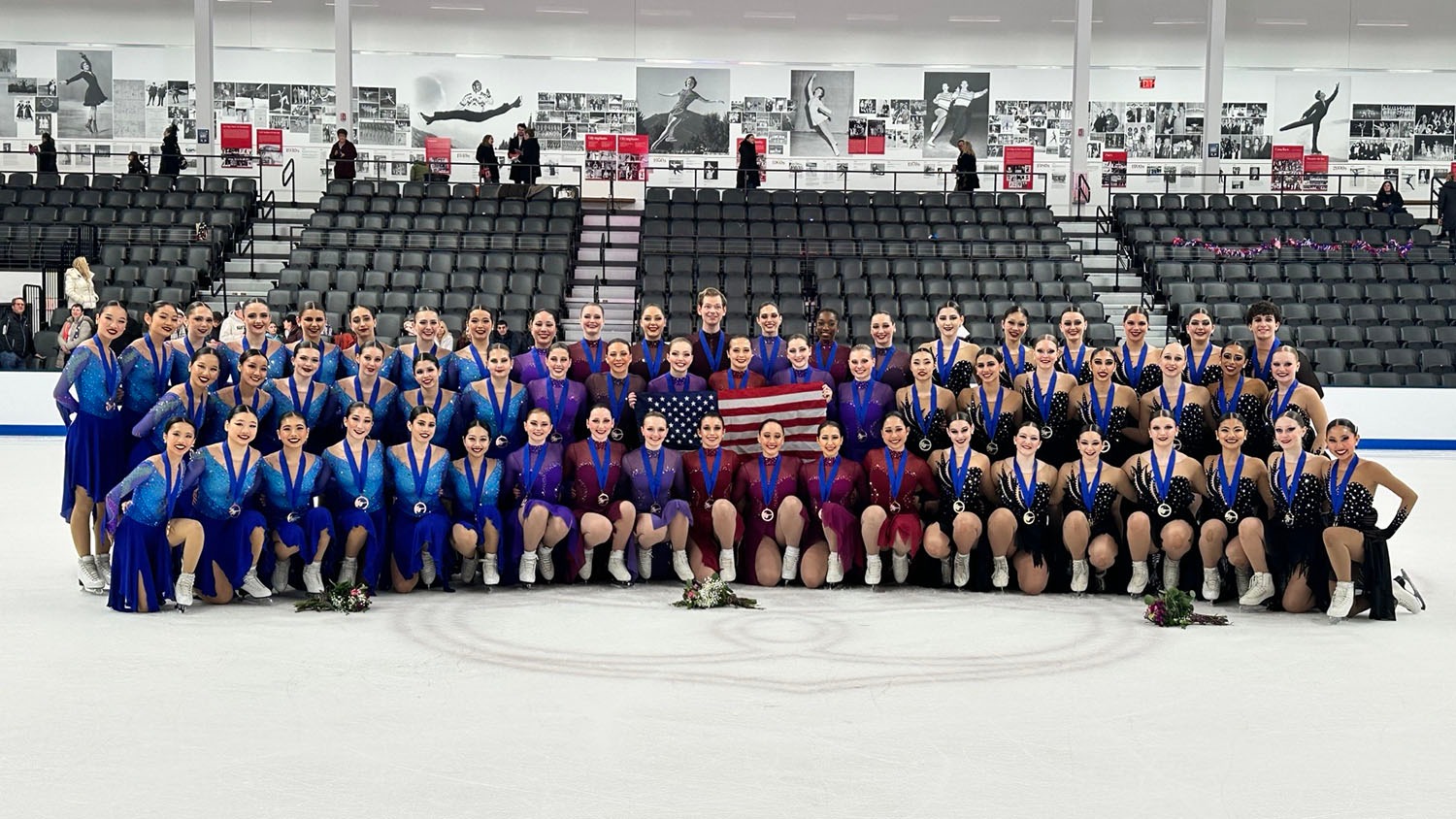 All three U.S. teams that medaled at the 2025 U.S. Synchronized Skating International Classic pose for a photo together on the ice at The Skating Club of Boston. On the left, in blue dresses with sparkly blue tops and wearing the junior bronze medal is Skyliners junior. The Haydenettes are in the center, wearing bronze medals and costumes that are different shades of purple and red. On the right is Teams Elite, which won gold in the junior competition. They wear black dresses with jewels on the top.