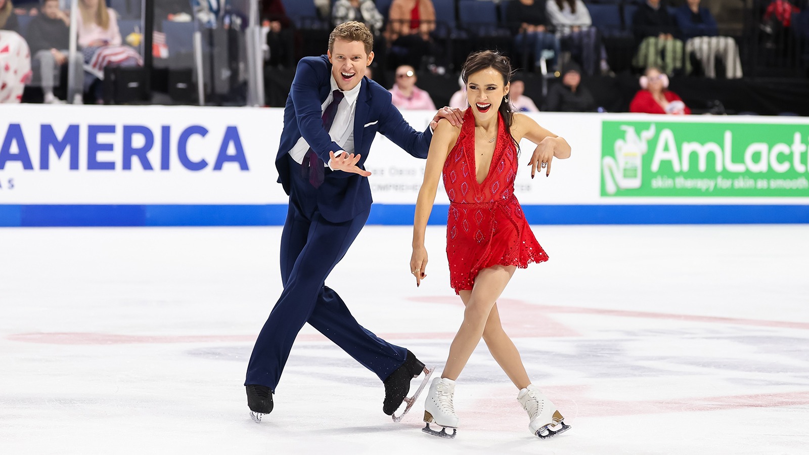 Madison Chock, dressed in red, and Evan Bates, dressed in a blue suit, playfully perform their rhythm dance.