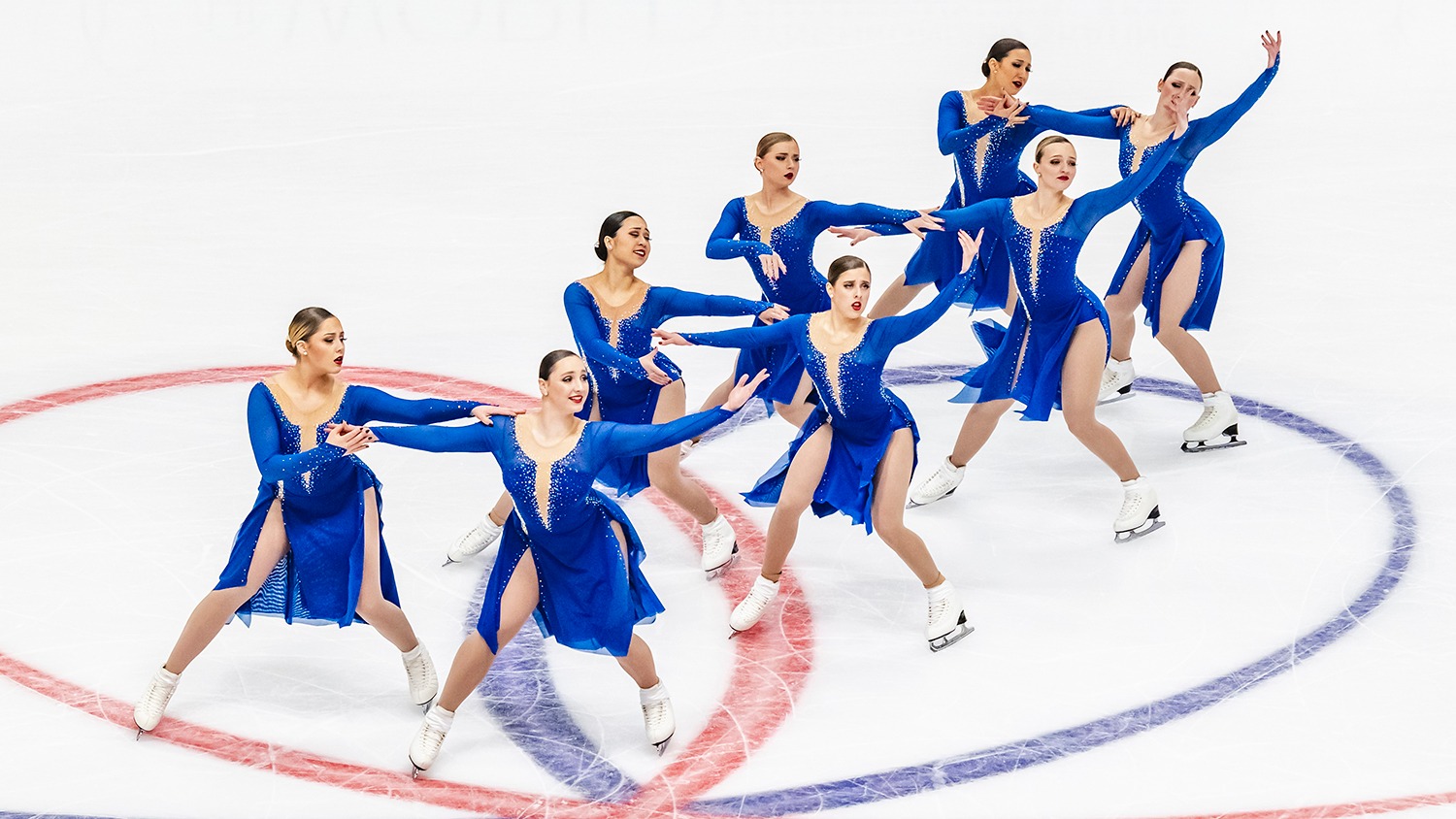 Eight Haydenettes skaters, in four groups of 2 that are staggered diagonally, skate in royal blue dresses at the World Synchronized Skating Championships. 
