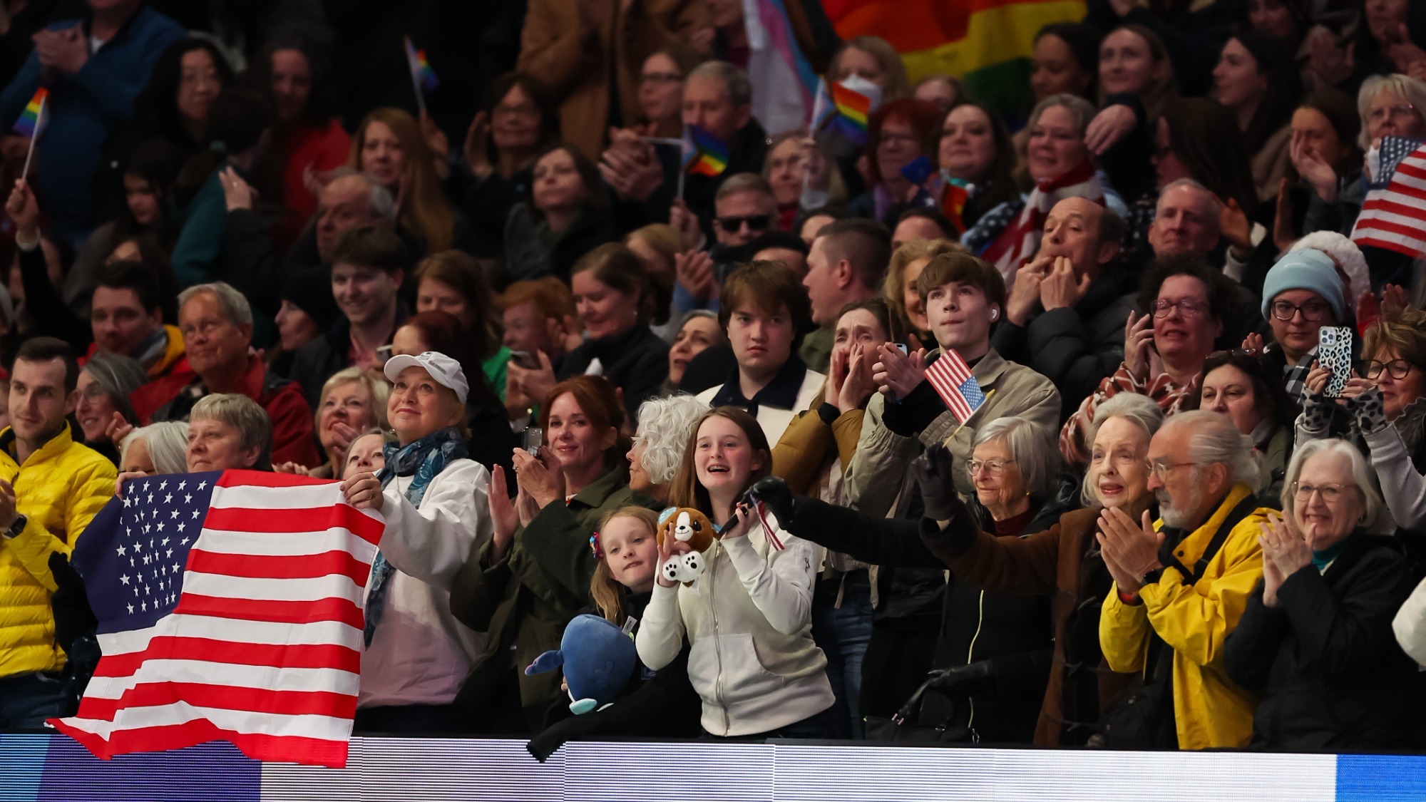 Photo of the crowd cheering at an event. One person in the front row is holding a U.S. flag